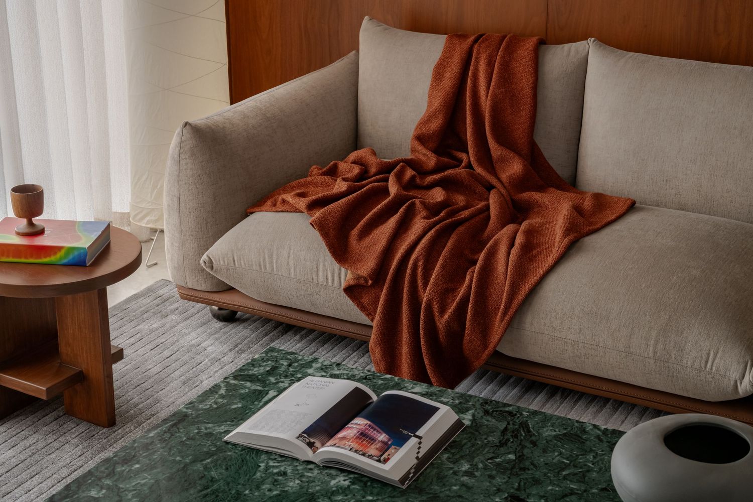 Close-up of beige sofa with draped rust throw blanket, open magazine, and green marble coffee table.