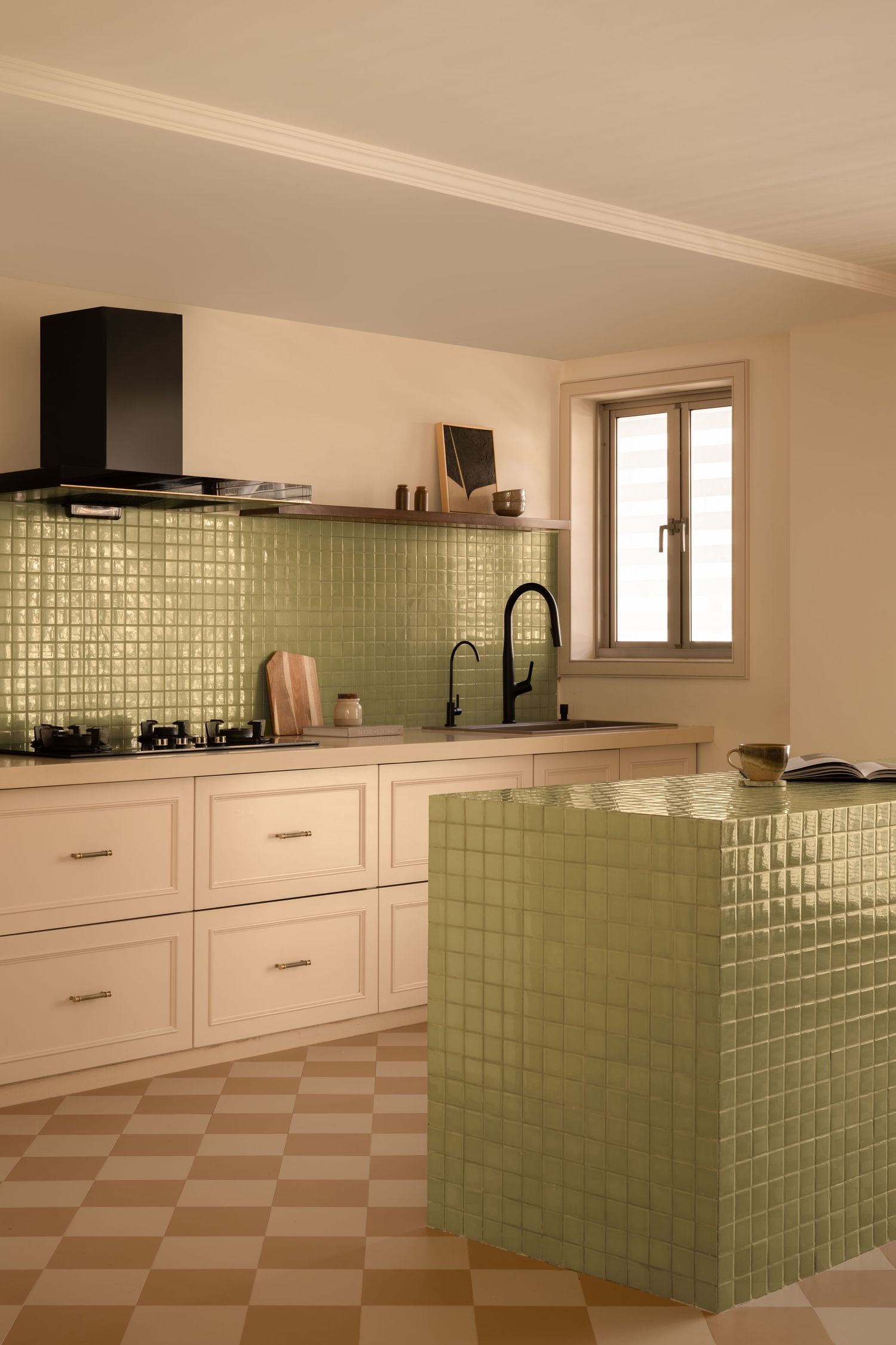 Stylish kitchen with sage green mosaic tile backsplash, cream cabinetry, black fixtures, and checkered floor.