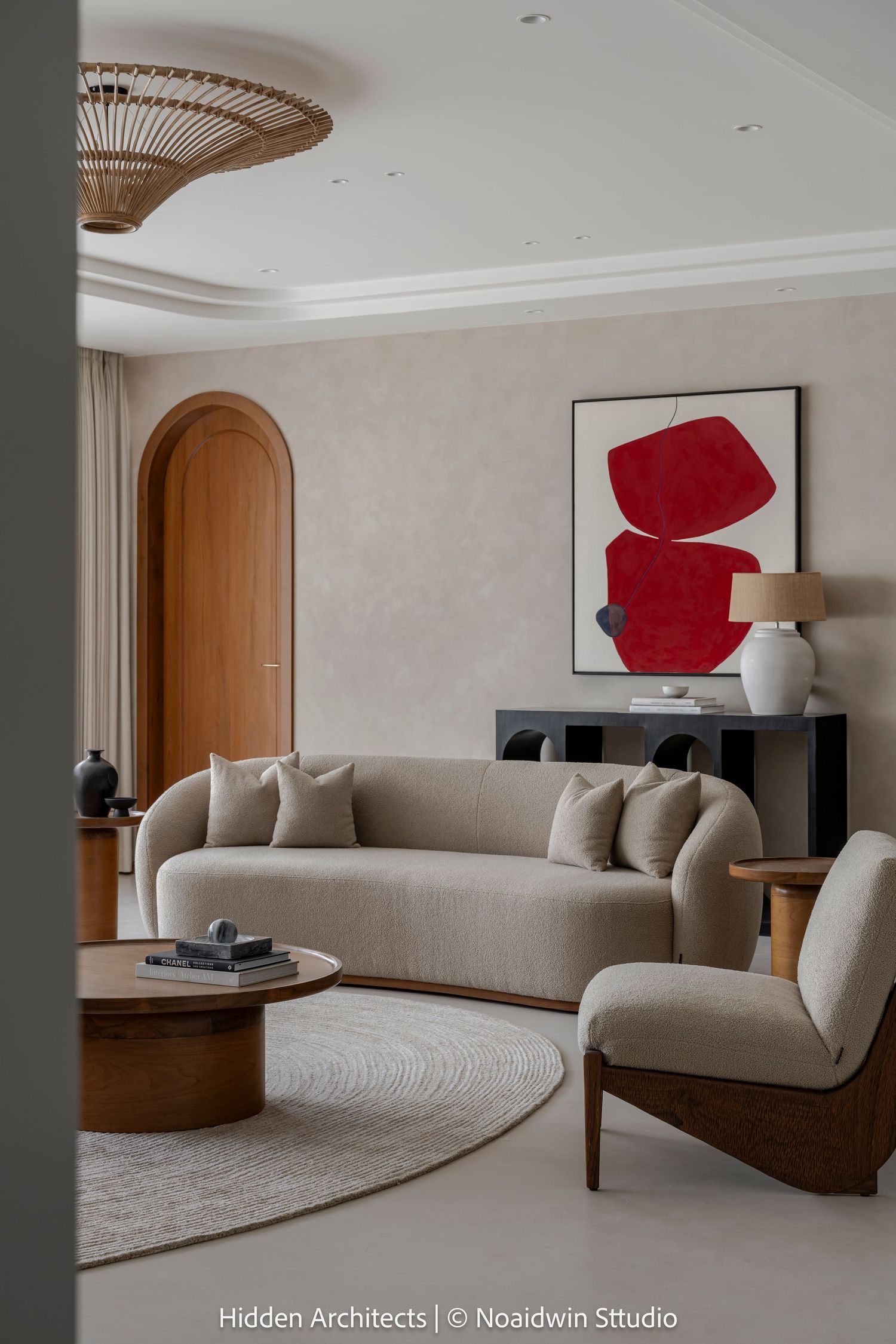 Elegant living room with curved beige sofa, round wood coffee table, red abstract artwork, and arched doorway in neutral tones.