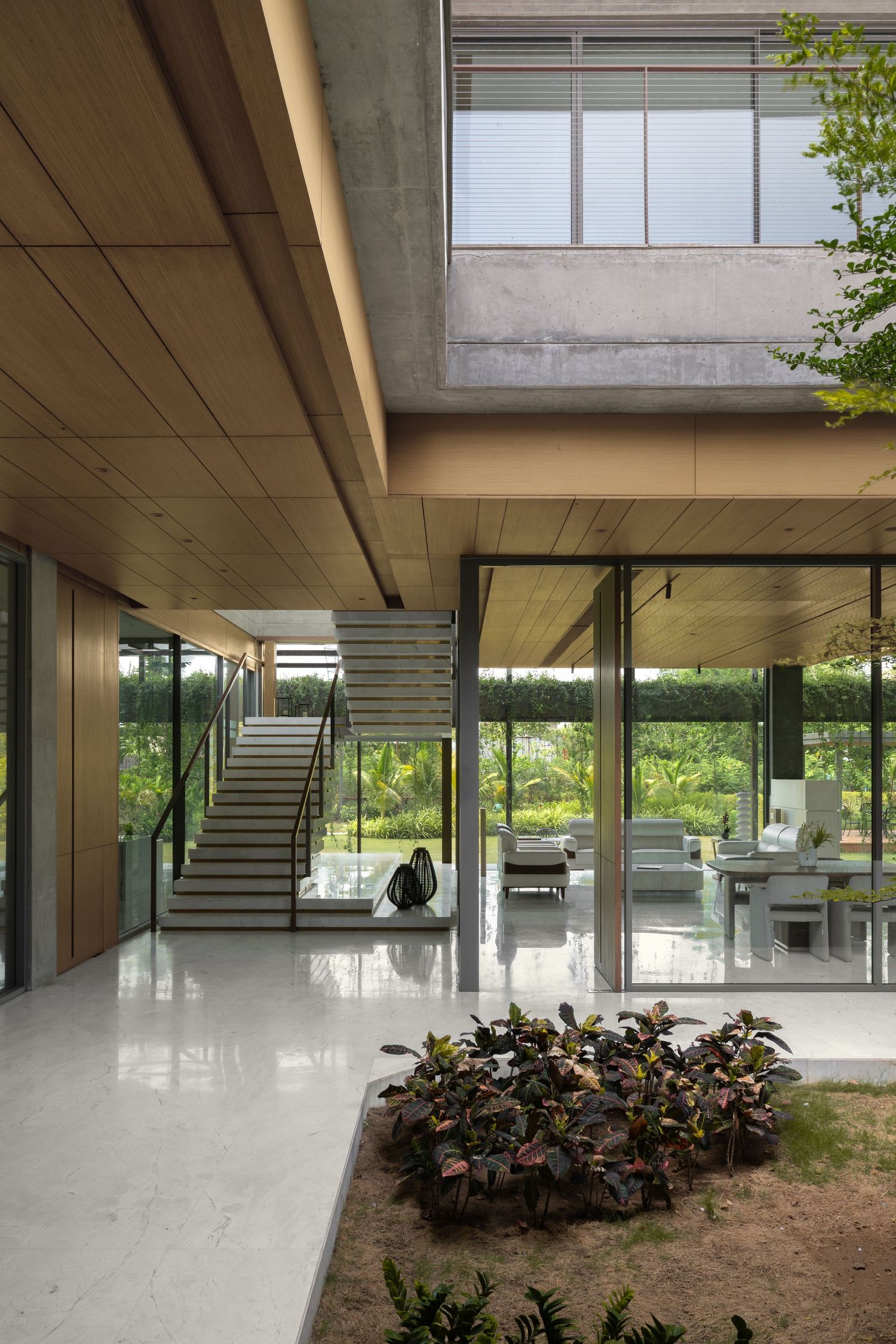 Modern open-plan home with marble floors, wood ceilings, glass walls, staircase, and lush garden views.