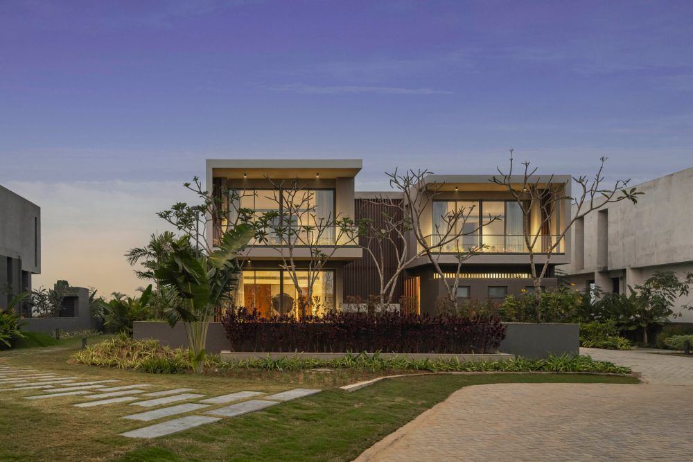Elegant two-story contemporary home with warm interior lighting and mature trees at dusk.