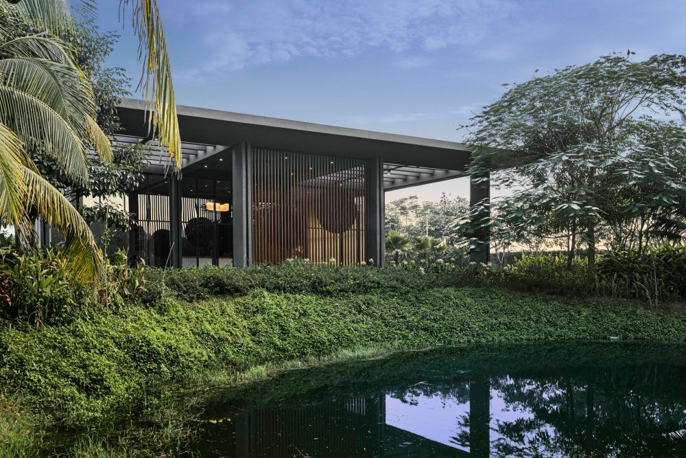 Sleek modern pavilion surrounded by tropical greenery reflected in a serene pond in a lush landscape setting.