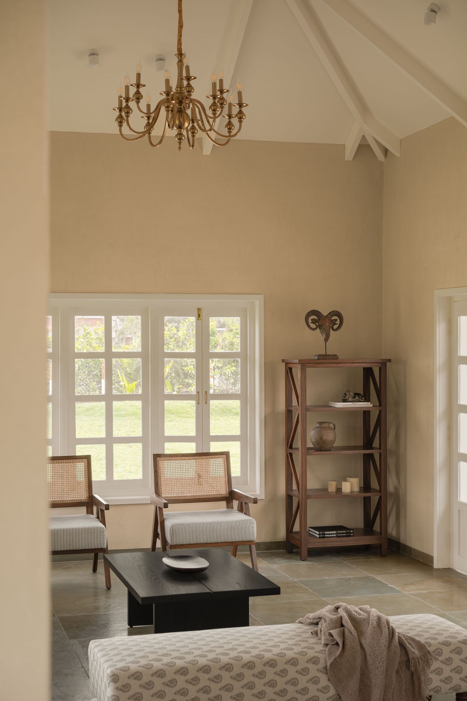 Bright farmhouse living room with vaulted ceiling, brass chandelier, cane chairs, and wooden bookshelf.