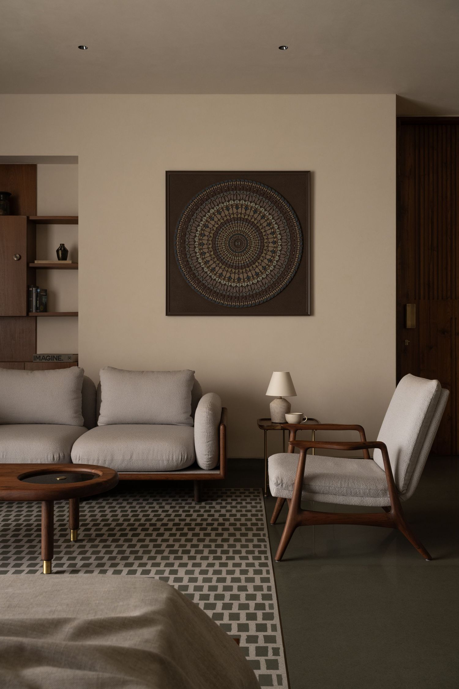 Cozy living room featuring gray linen sofas, wooden armchair, mandala wall art, and geometric patterned area rug.