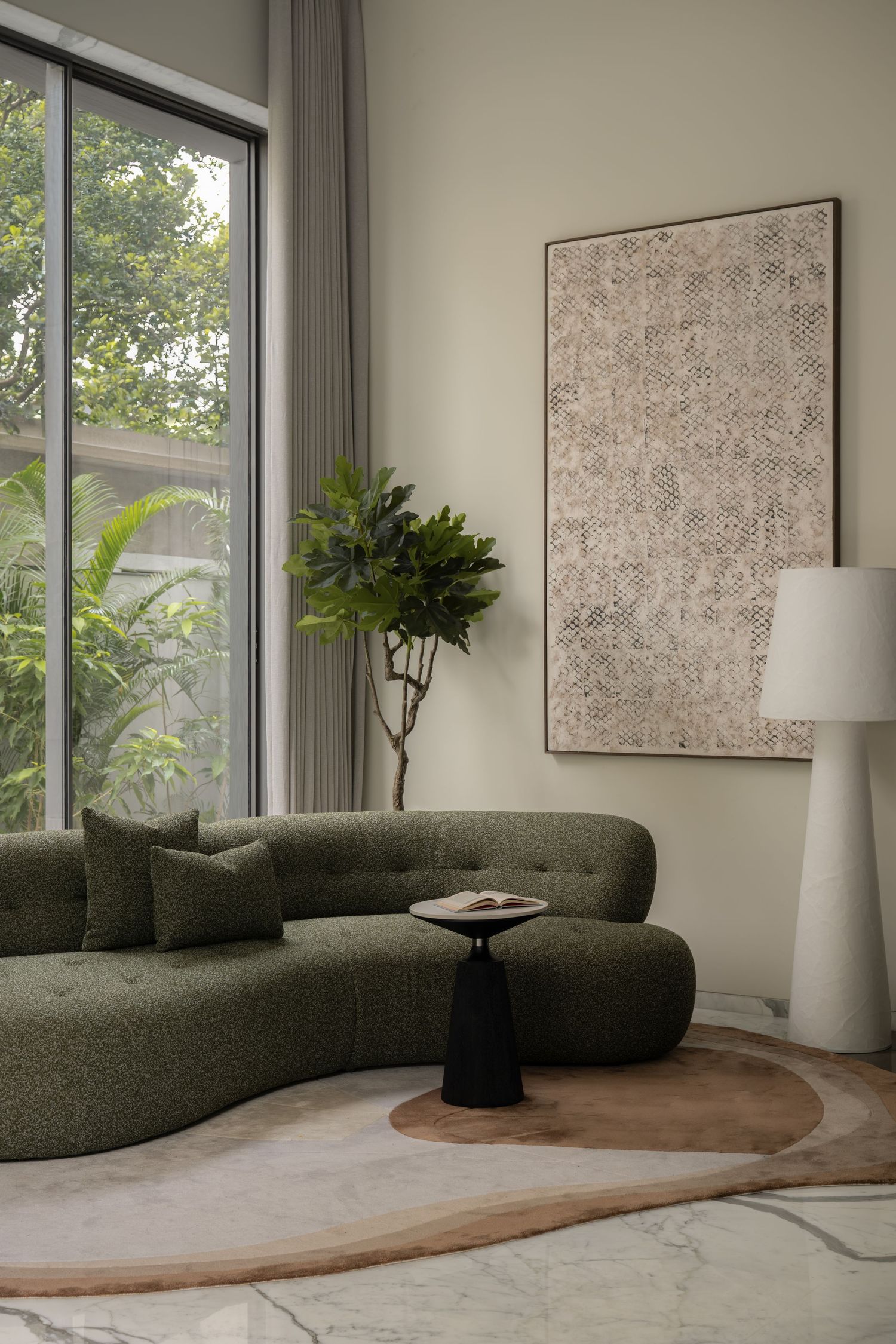 Modern living room with curved green sofa, abstract wall art, fiddle leaf fig plant, and floor lamp by large window.