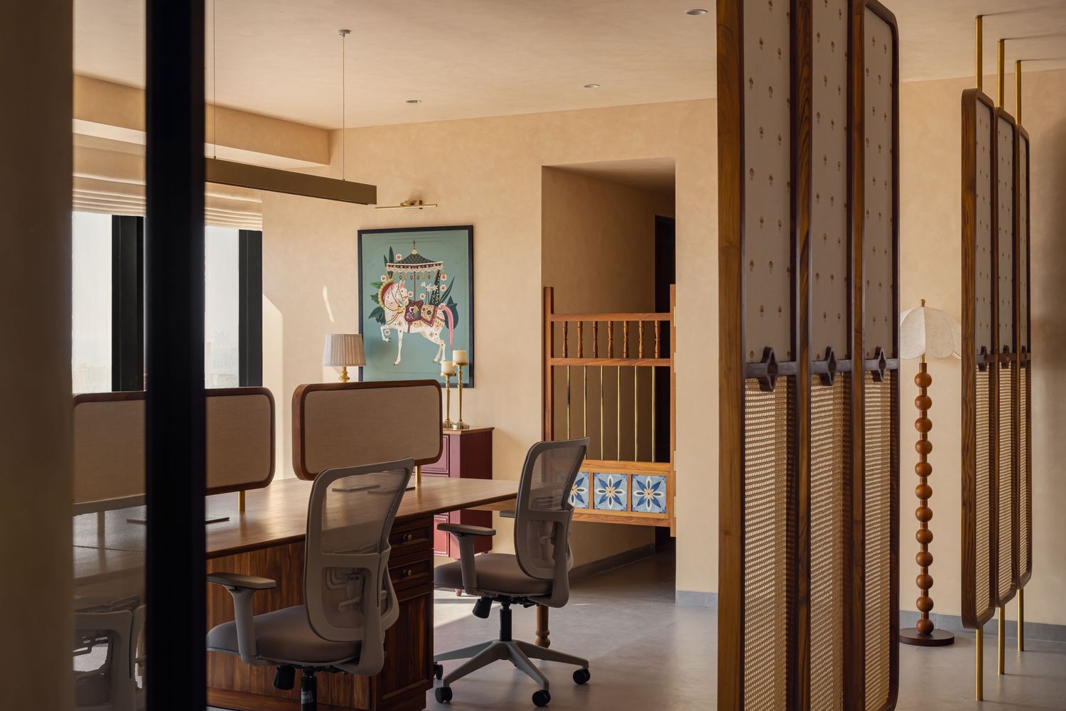 Modern workspace with mesh office chairs, wooden desk, decorative screen divider, and colorful artwork in warm beige tones.