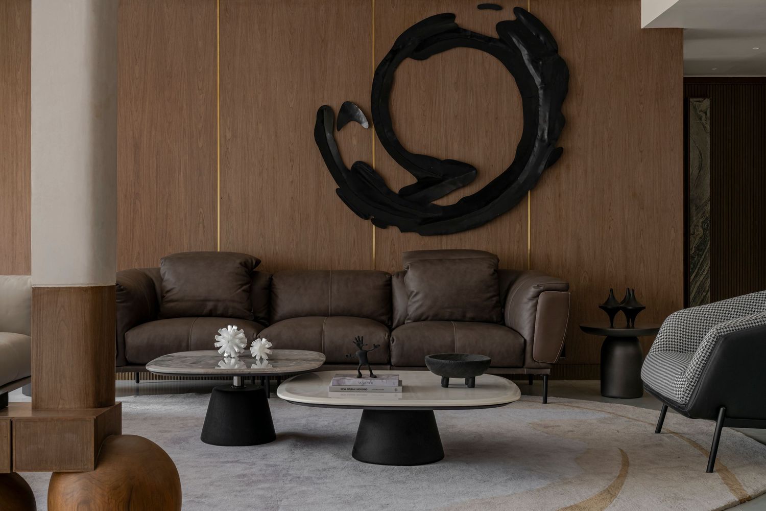 Sophisticated living room with brown leather sofa, circular black wall art, and marble coffee tables on a neutral rug.