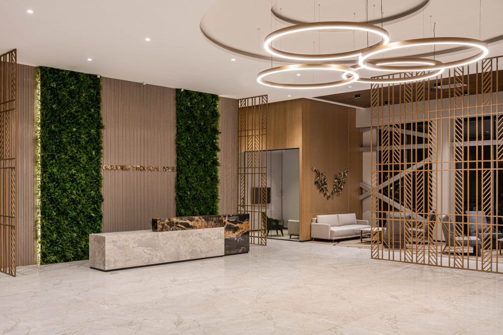 Luxury hotel reception with green moss wall, marble front desk, circular chandeliers, and gold lattice room dividers.