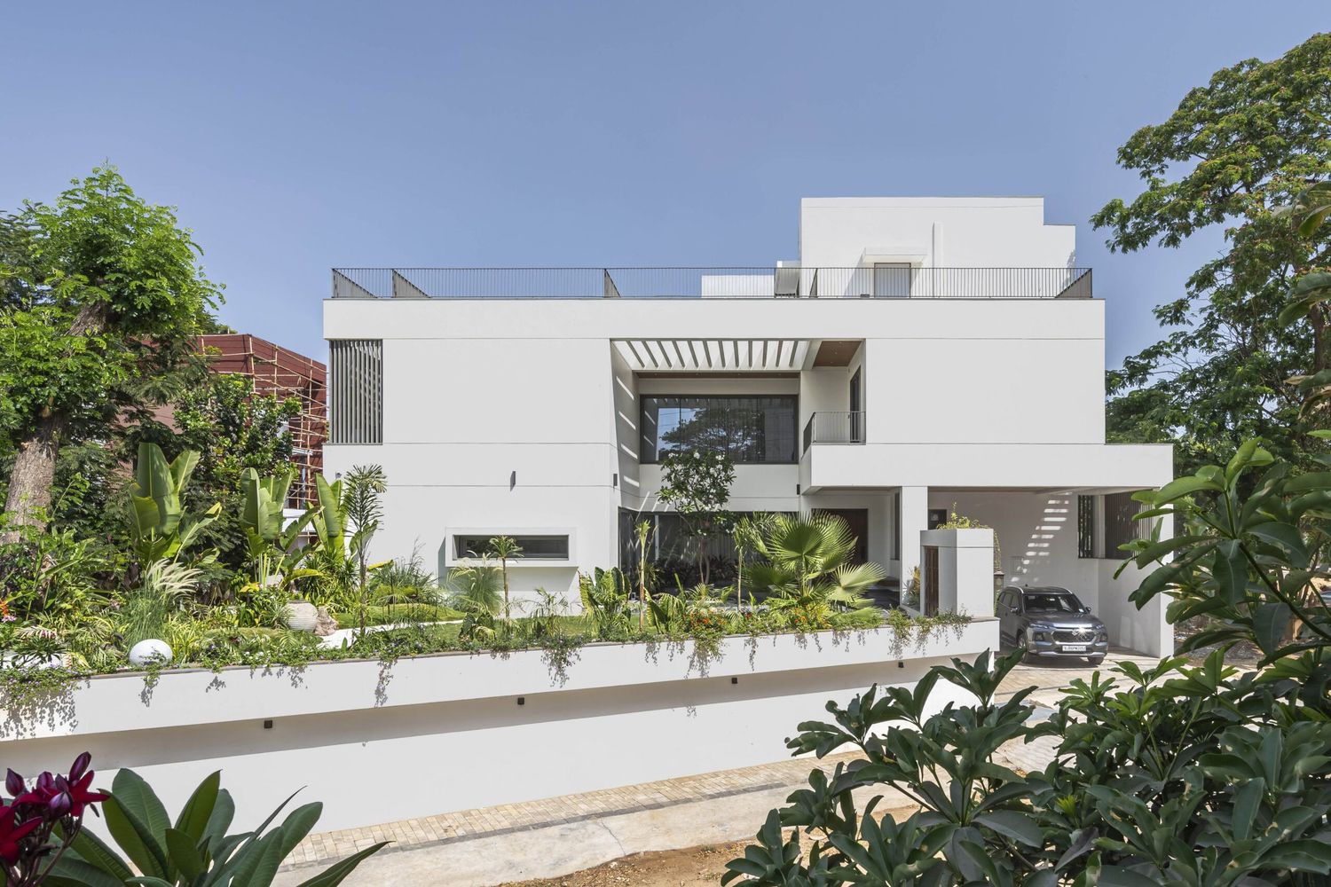 Bright white contemporary villa with flat roof, lush garden, and open terrace design.