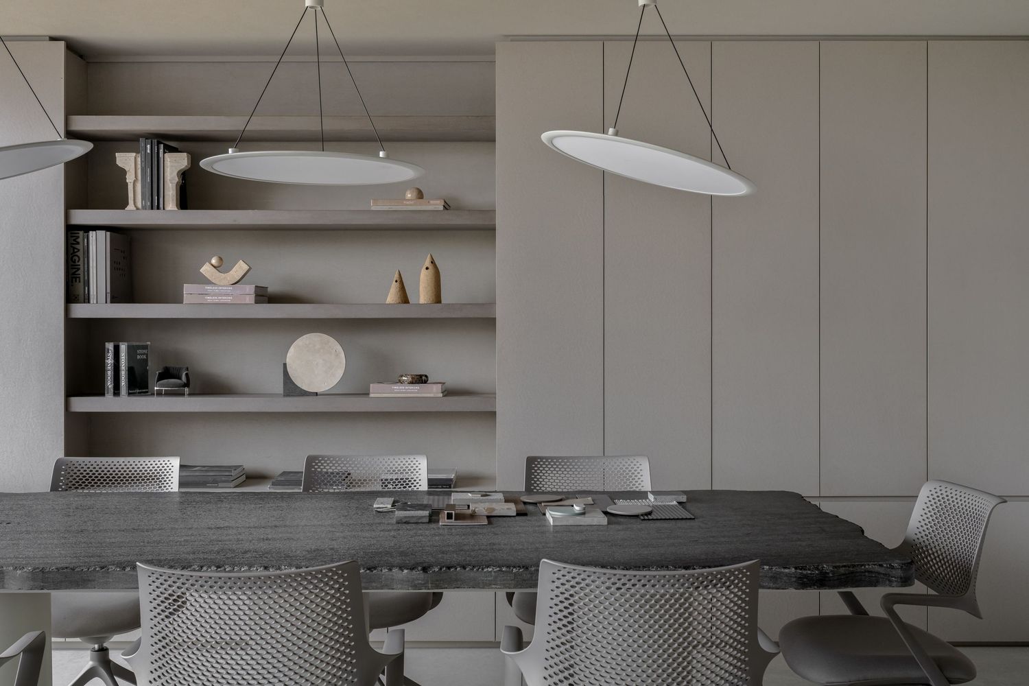 Modern gray dining room with oval pendant lights, a stone table, upholstered chairs, and built-in shelving with decor.
