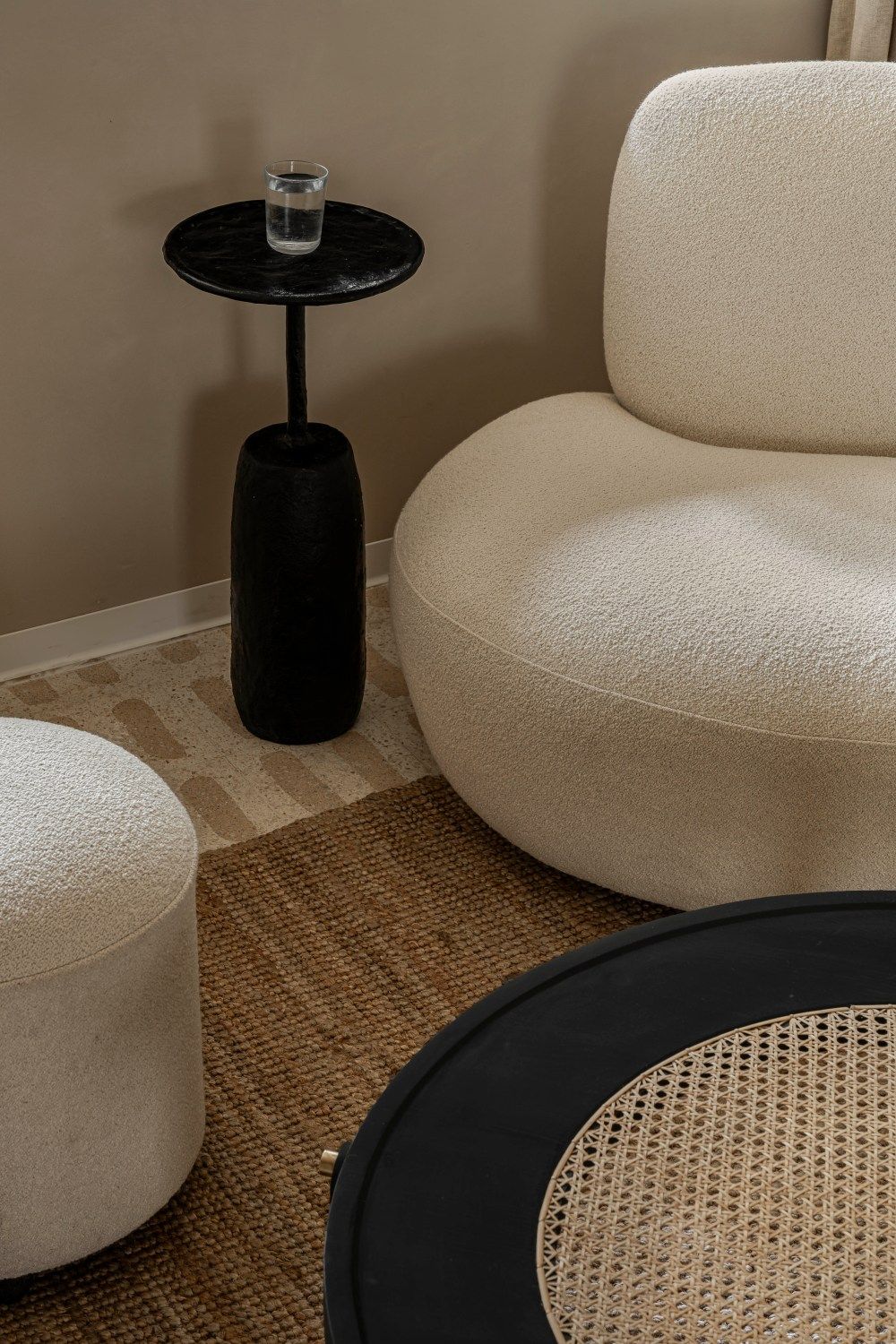 Close-up of white boucle armchair, black marble side table, woven rug, and rattan coffee table in neutral interior.
