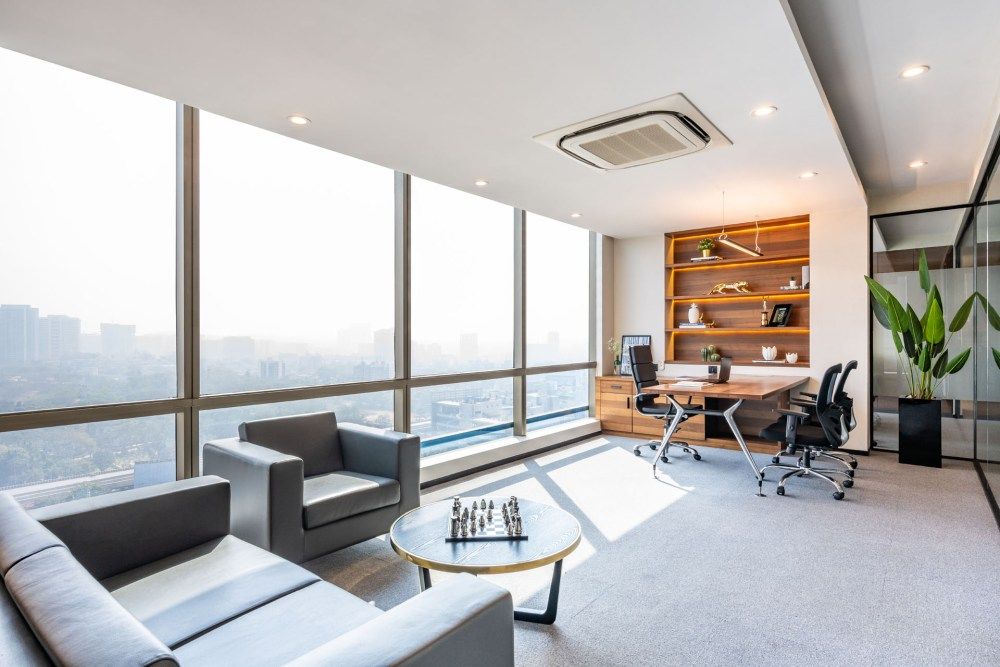 Sun-filled executive office suite with panoramic city views, wooden furniture, built-in shelving, and comfortable lounge seating.