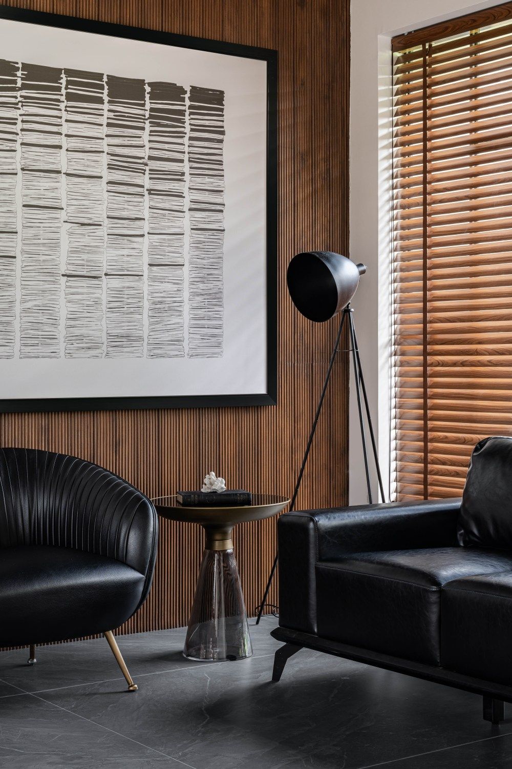 Elegant office lounge with black leather chairs, industrial floor lamp, wood panel wall, and large abstract artwork.
