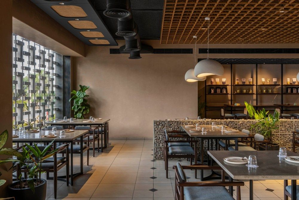 Stylish modern restaurant with lattice ceiling, decorative brick wall, pendant lights, and lush plants.