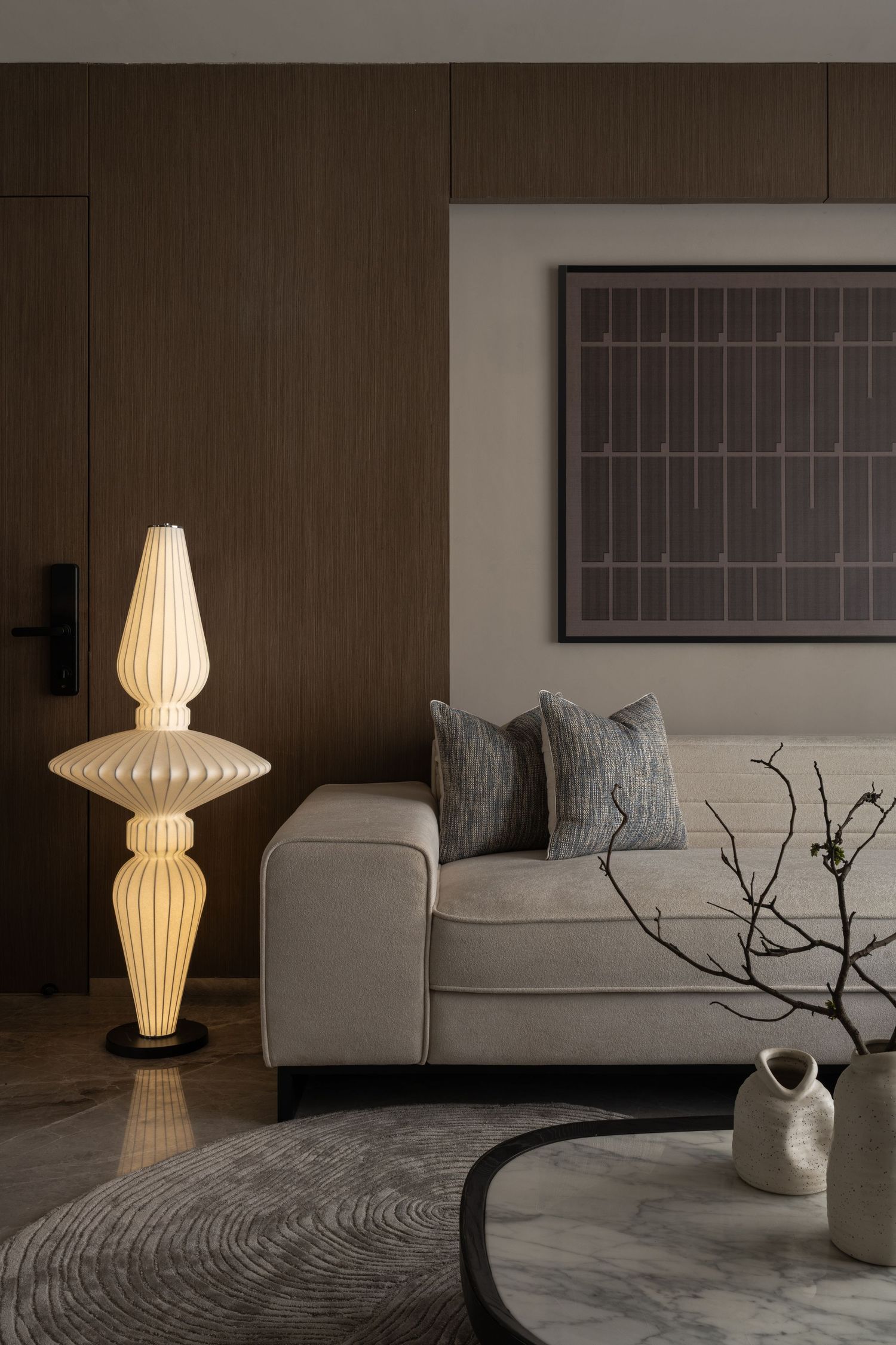 Elegant living room with sculptural floor lamp, beige sofa, framed artwork, and decorative branch vase.