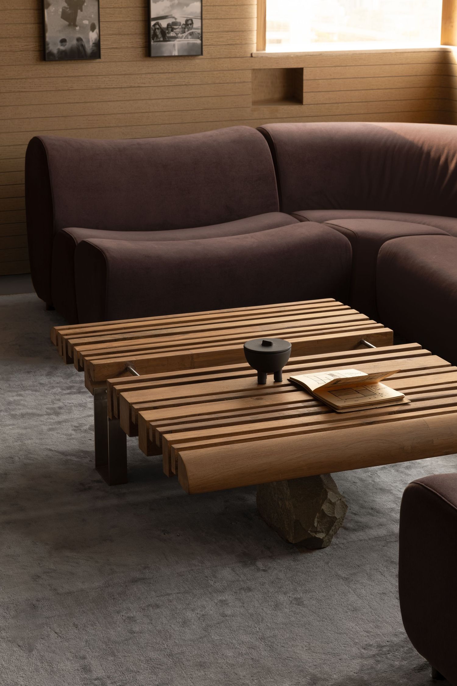Brown curved sectional sofa with wooden slatted coffee table on gray carpet in modern living room.