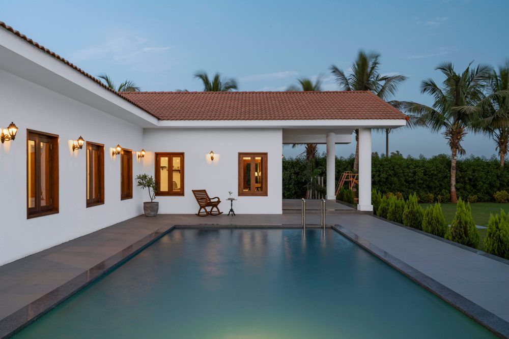 White villa with terracotta tile roof and illuminated swimming pool reflecting evening light at dusk.