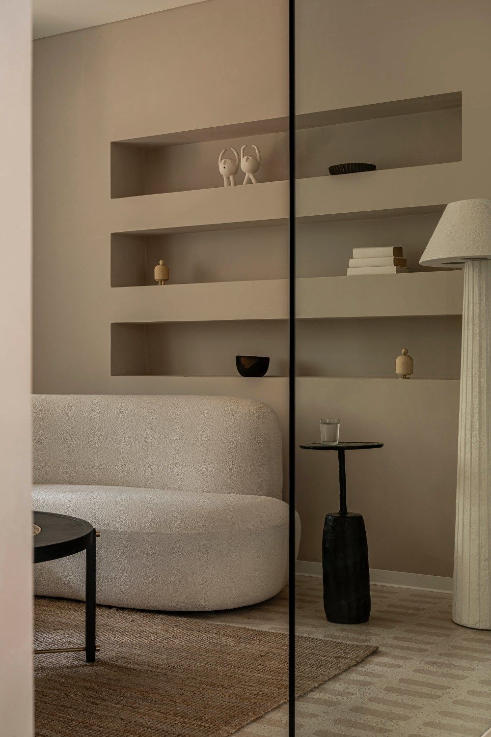 Cozy neutral lounge with curved white sofa, built-in shelving, black side table, and floor lamp.
