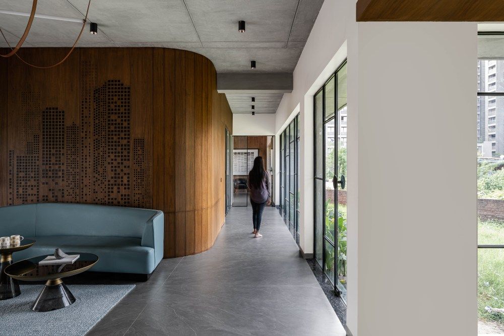 Modern office corridor with curved carved wood feature wall, blue seating area, and glass exterior windows.