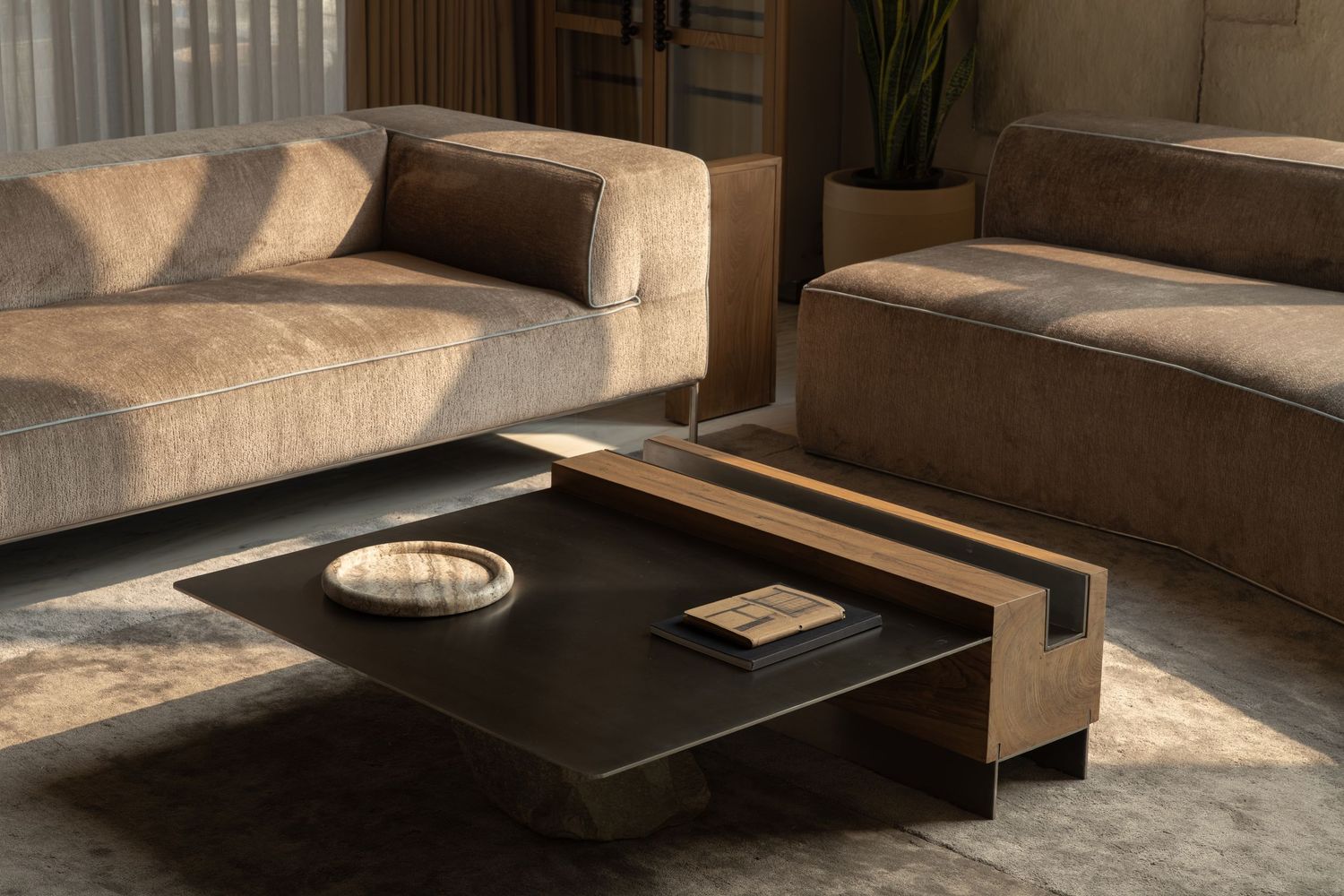 Close-up of beige velvet sofas with a sleek black and wood rectangular coffee table in warm natural light.