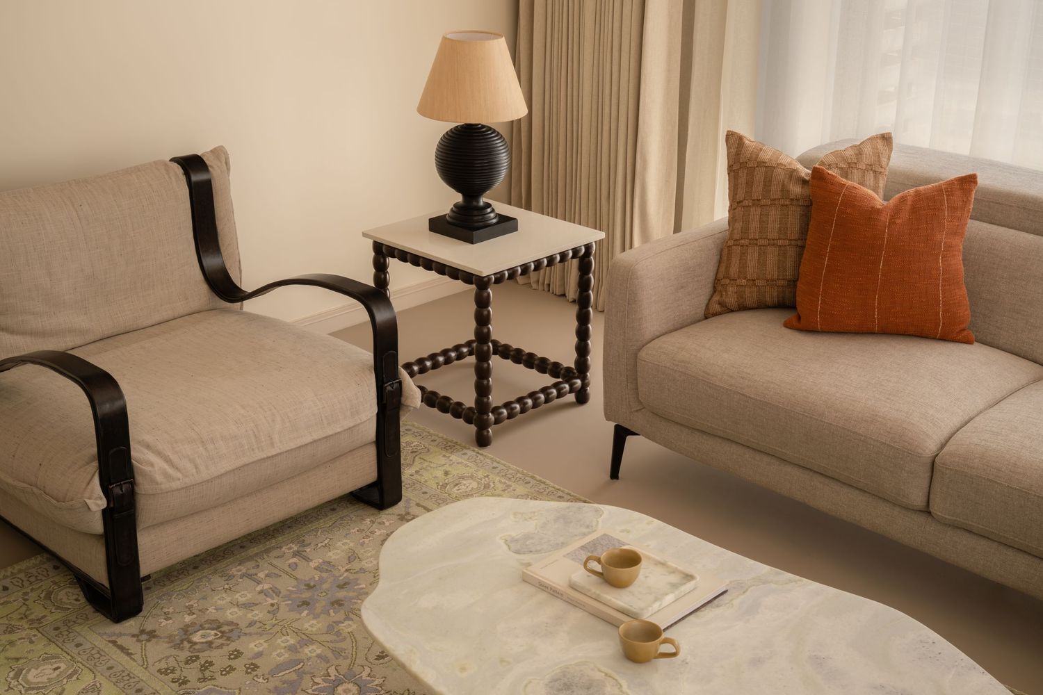 Minimalist living room with beige sofa, black accent chair, marble coffee table, and warm lamp.