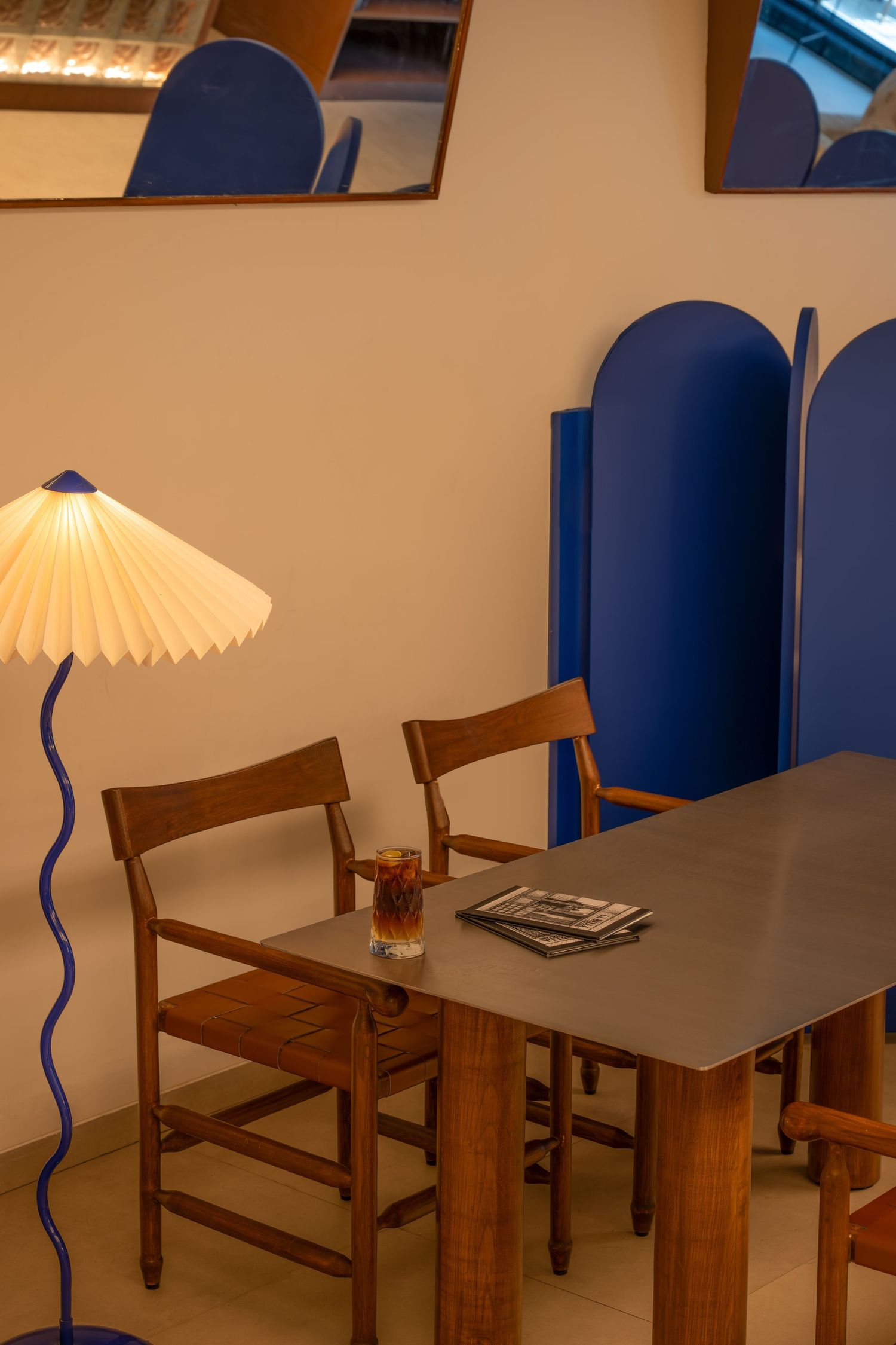 Retro dining area with blue wavy floor lamp, wooden table, chairs, and bold blue room divider.