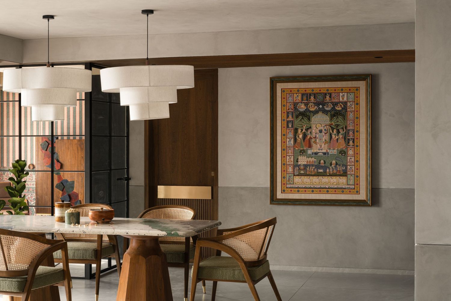 Contemporary dining space featuring round table, wooden chairs, white pendant lights, and traditional framed artwork.