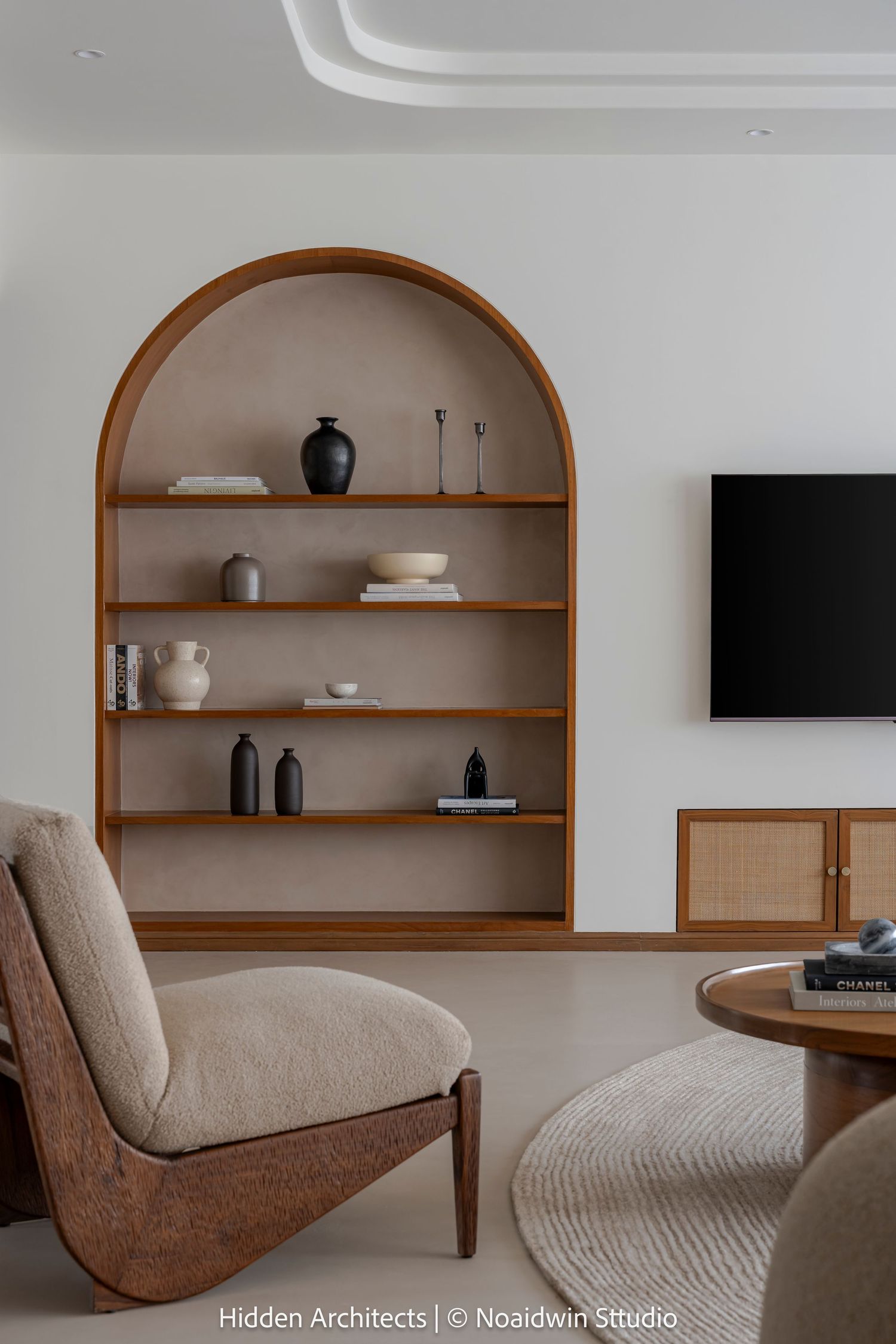 Cozy living room with arched built-in wood shelving, decorative ceramics, bouclé armchair, and round walnut coffee table.