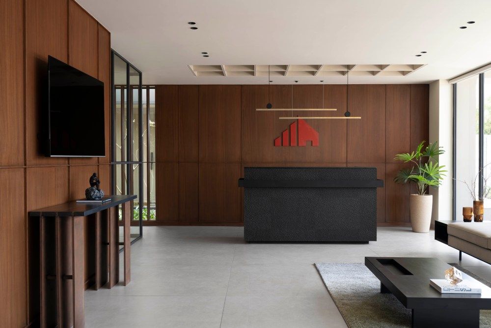 Contemporary corporate reception area with dark wood paneling, black reception desk, red logo, and pendant lighting.