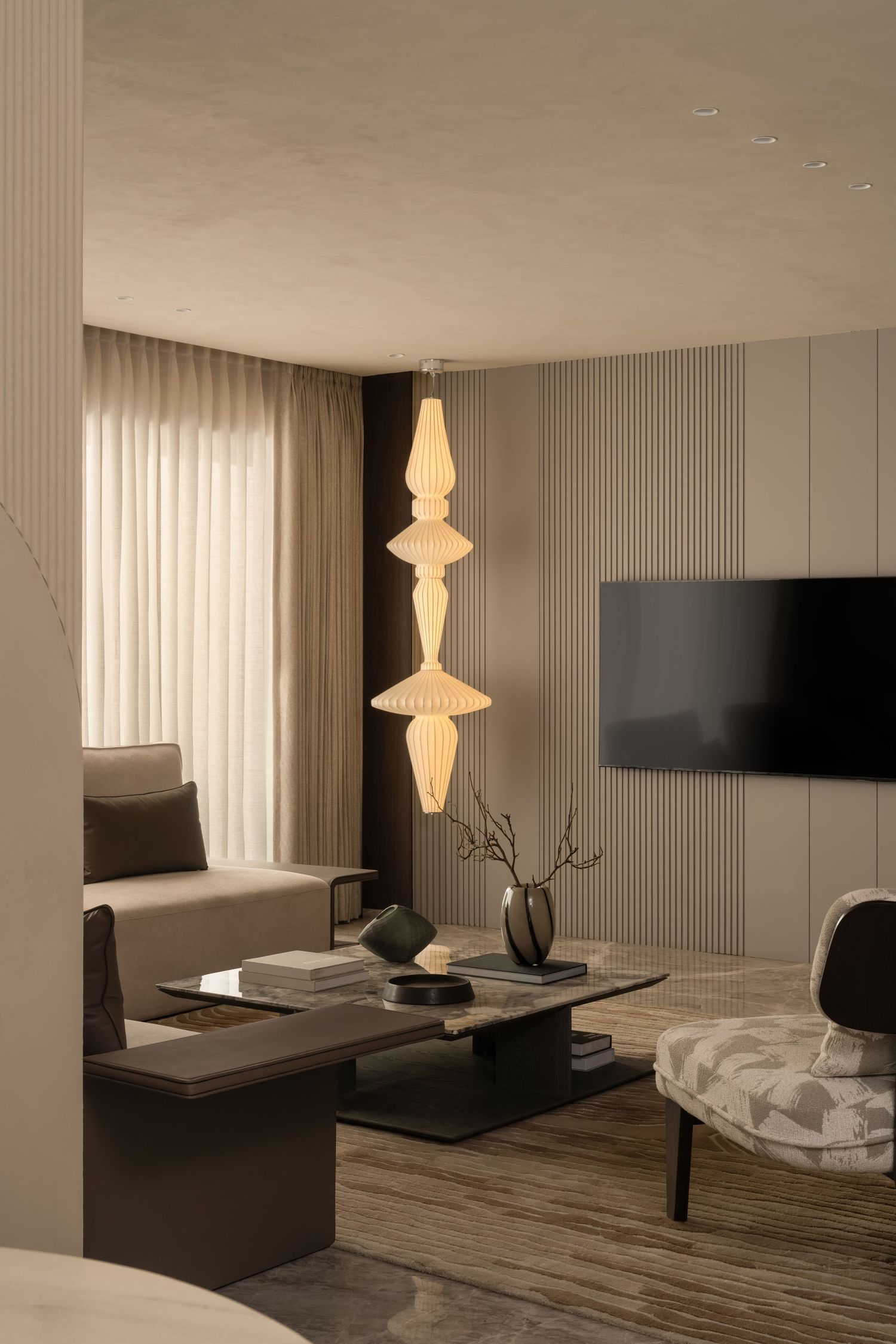 Modern living room with stacked ornate pendant lamp, neutral sofa, TV wall, and patterned accent chair.
