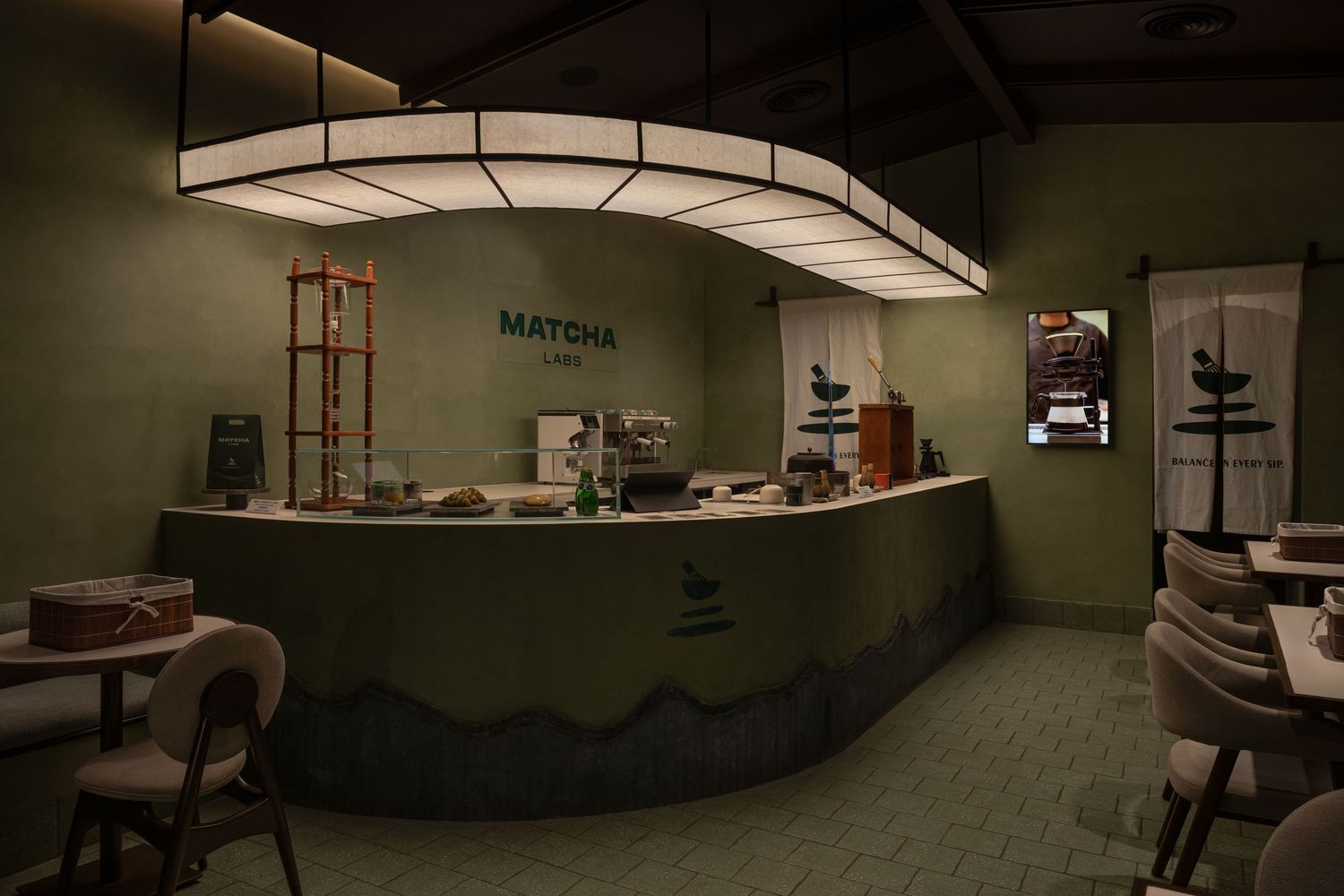 Modern matcha cafe interior with curved green counter, pendant lighting, and minimalist decor.