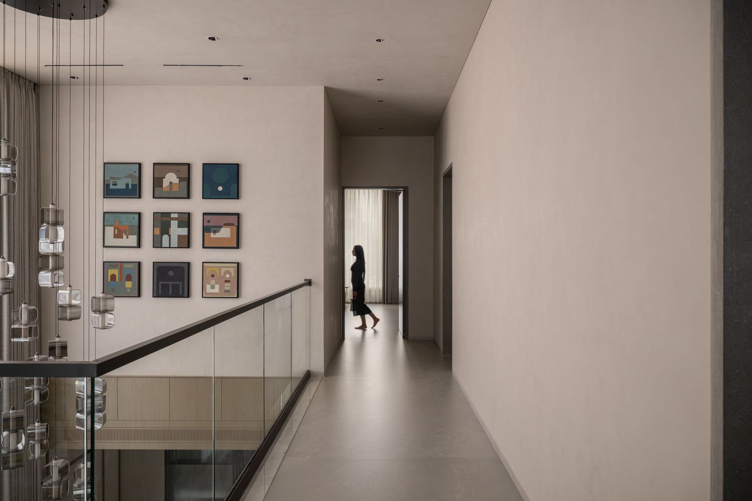 A silhouette of a person walking through a modern gallery hallway with framed artwork on white walls and glass railings.