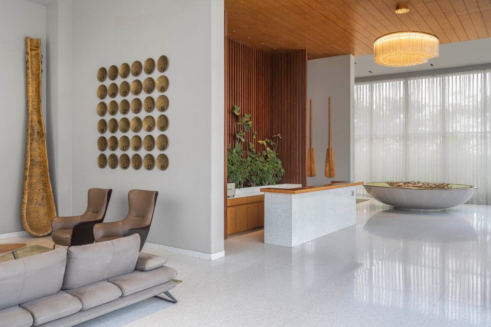 Elegant modern living space with wooden ceiling, circular stone basin, gold disc wall art, and neutral furnishings.