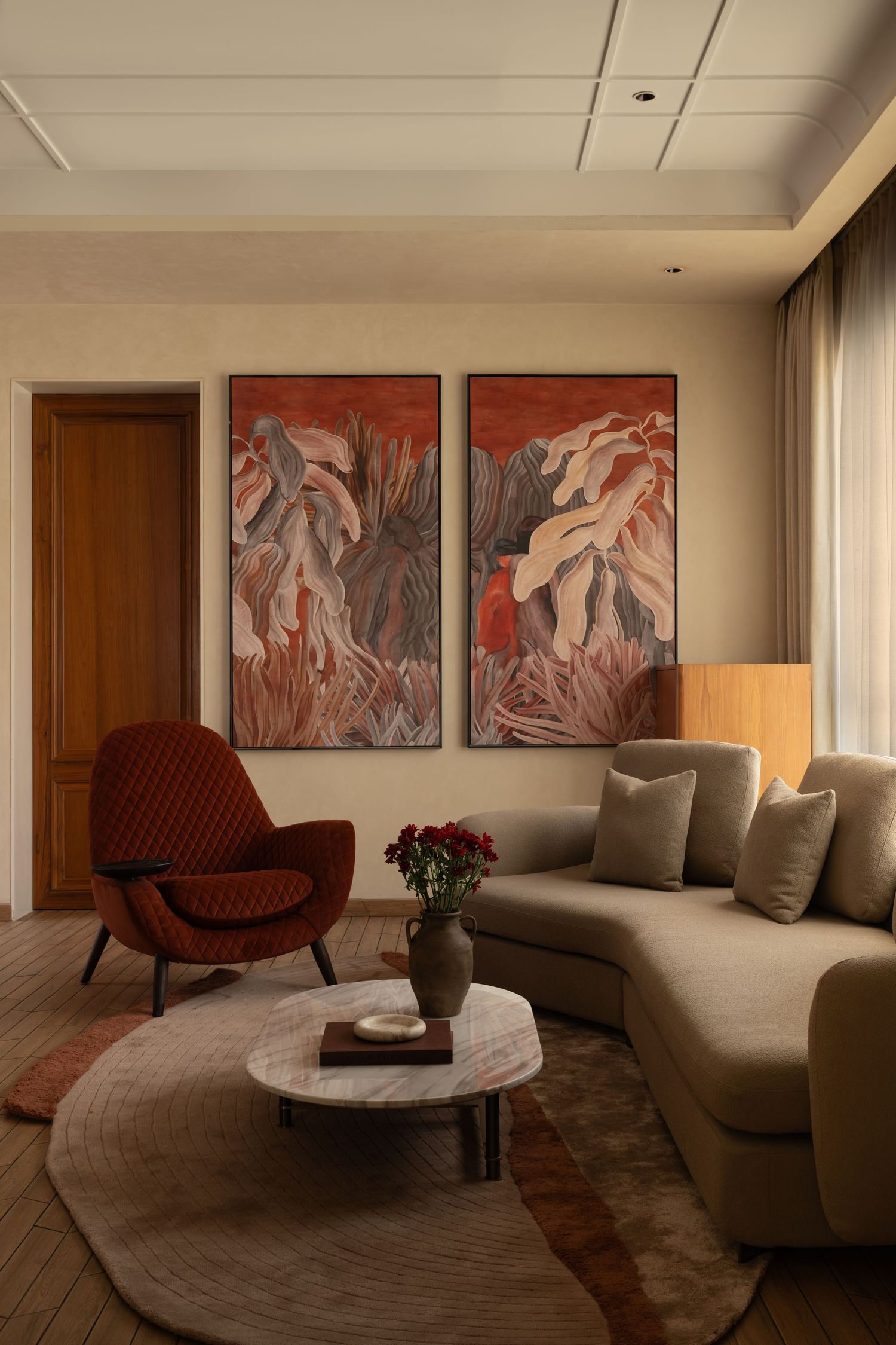 Modern living room with large abstract red artwork, beige sectional sofa, and rust velvet armchair.