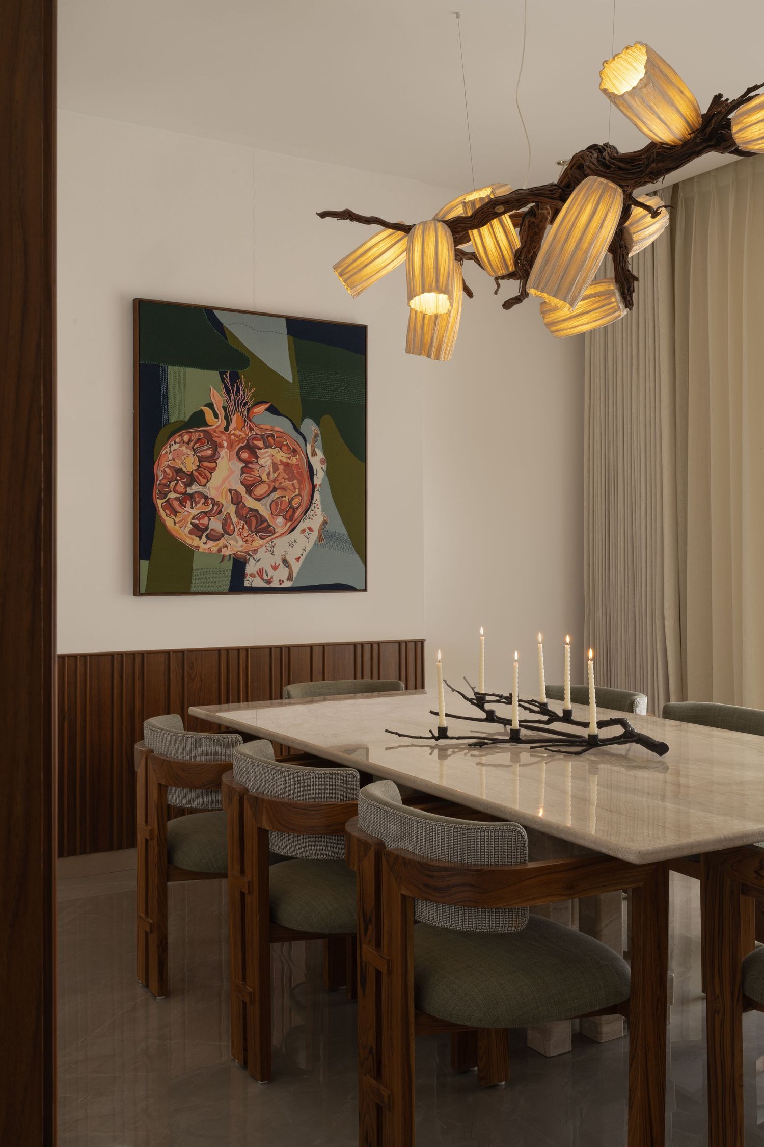 Sophisticated dining room with marble table, sage green chairs, branch chandelier, and pomegranate wall art.