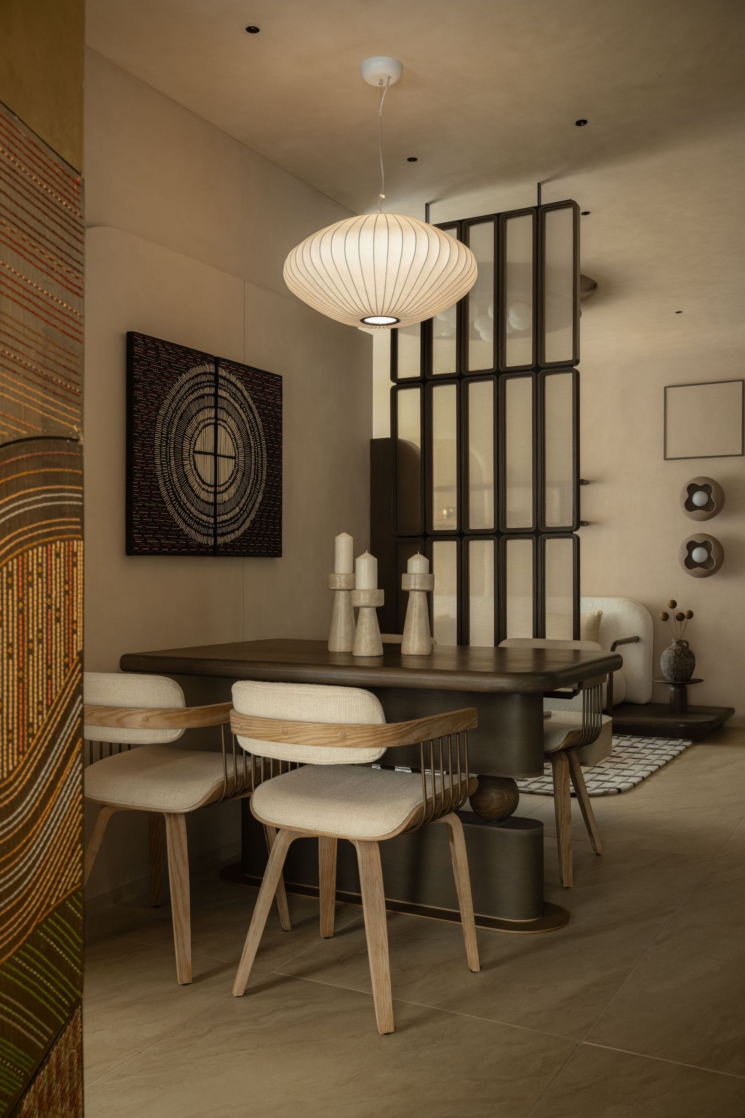 Modern dining room with wooden chairs, dark oval table, pendant light, and abstract wall art in neutral tones.