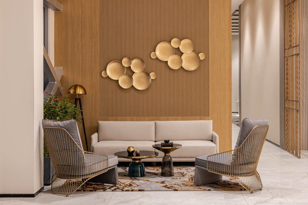 Contemporary lounge with beige sofa, woven armchairs, gold bubble wall art, and warm wood slat paneling.
