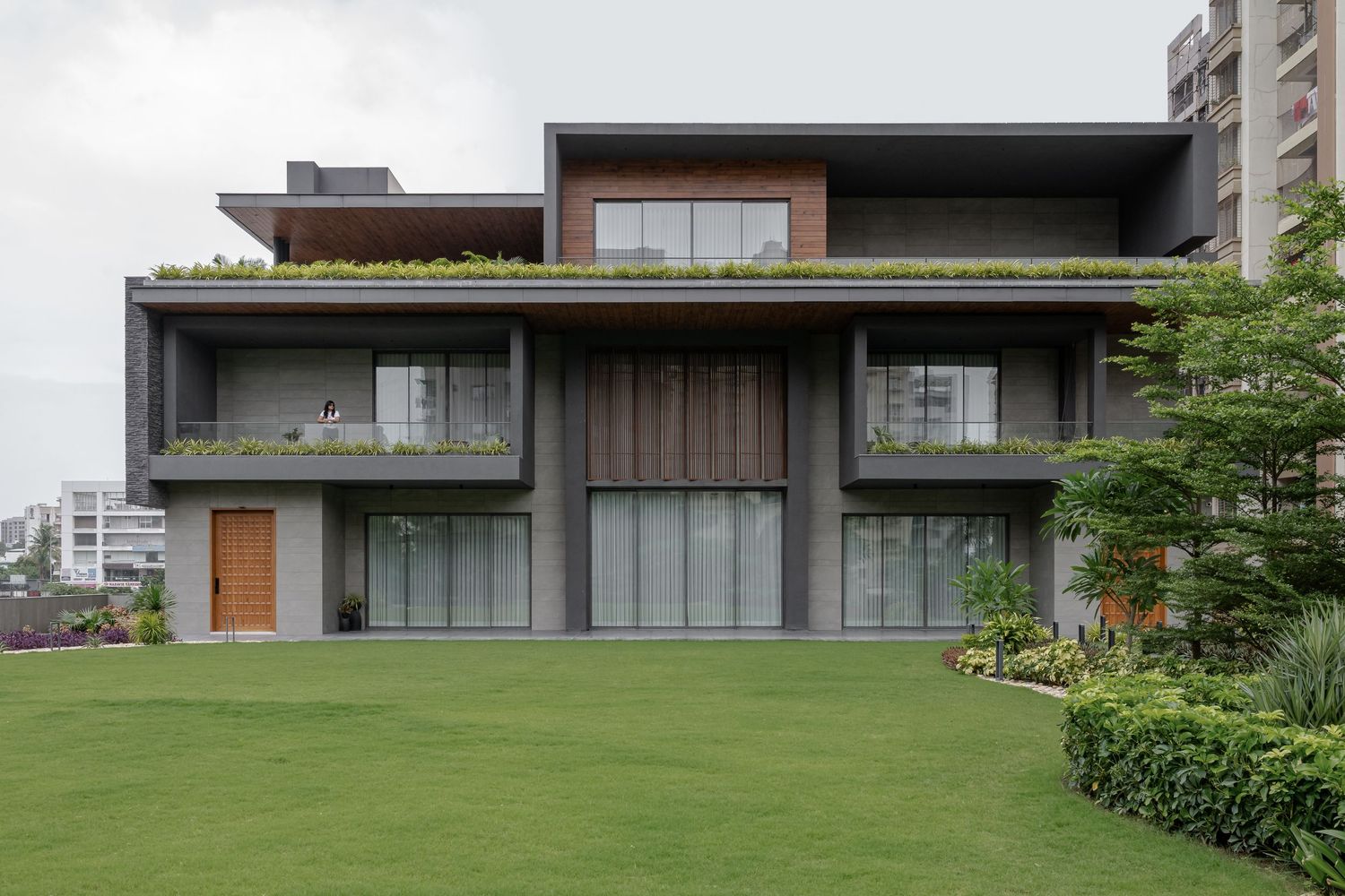 Modern two-story home with green rooftop garden, floor-to-ceiling windows, and lush lawn.
