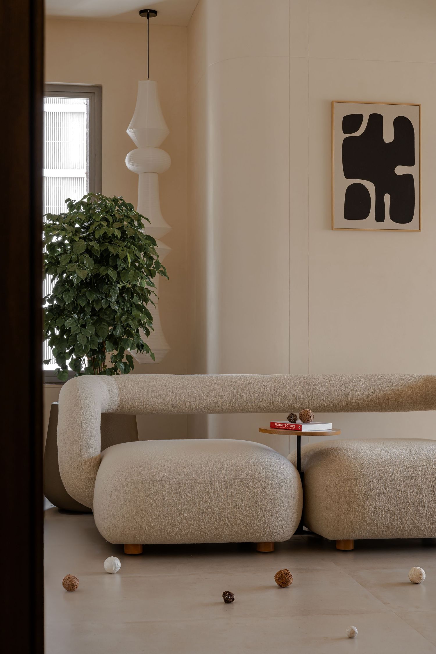 Minimalist living room with cream boucle sofa, sculptural white pendant, lush plant, and bold abstract black-white artwork.