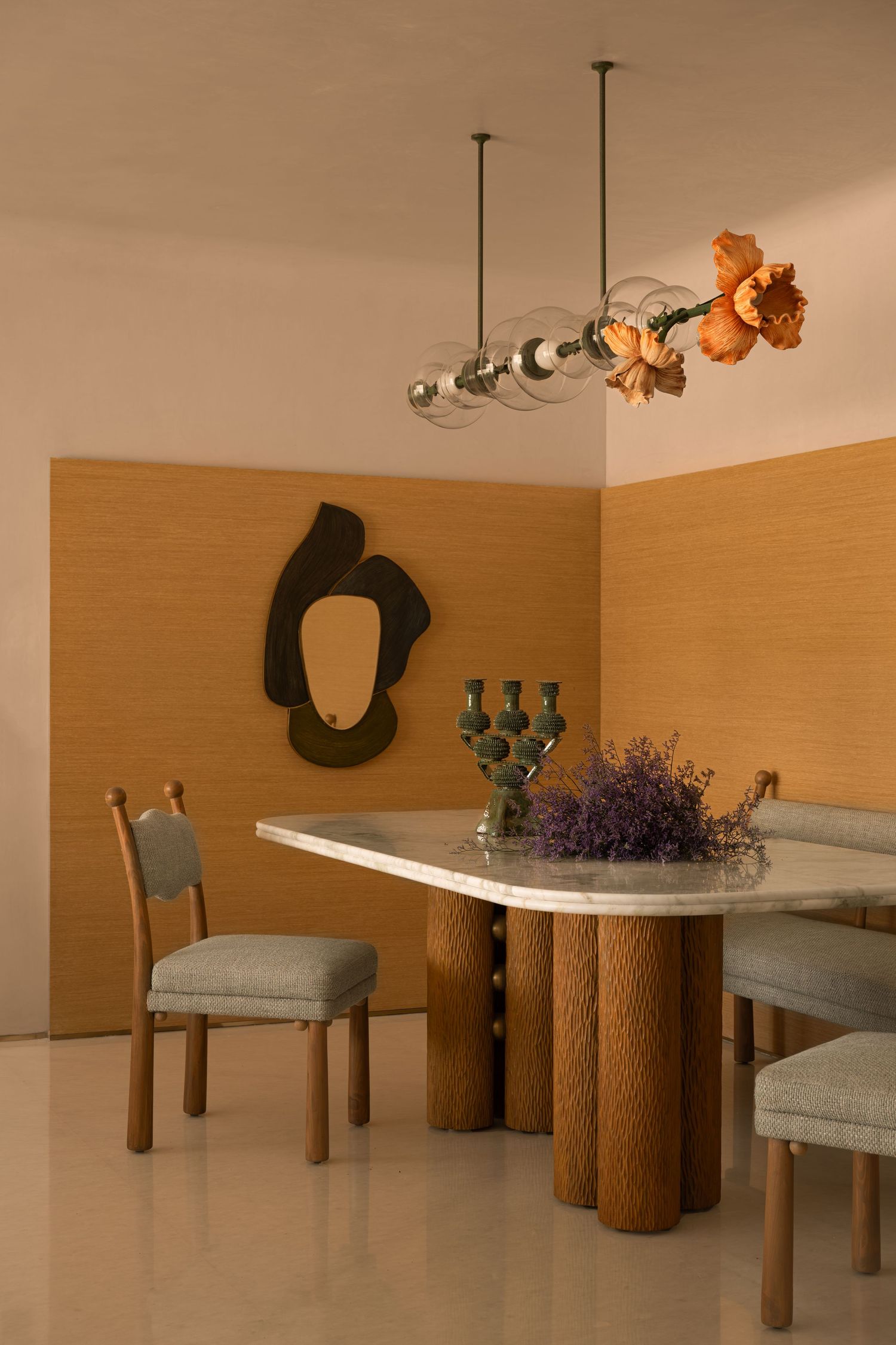 Elegant dining area with marble table, sculptural pendant light, orange floral arrangement, and wood wall panels.