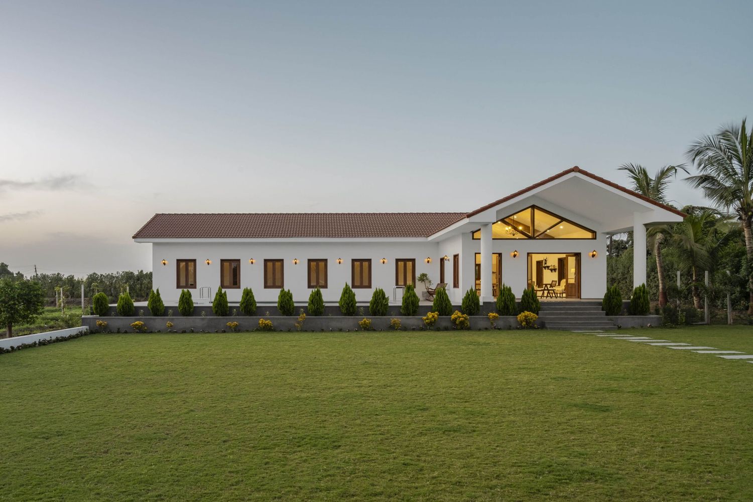 Elegant white rural building with terracotta roof glowing warmly at twilight surrounded by manicured gardens.