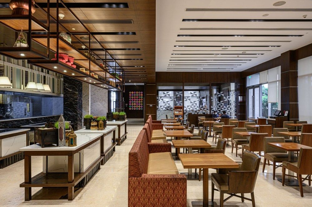 Modern restaurant interior featuring open kitchen, booth seating, wooden tables, and contemporary industrial-style decor.