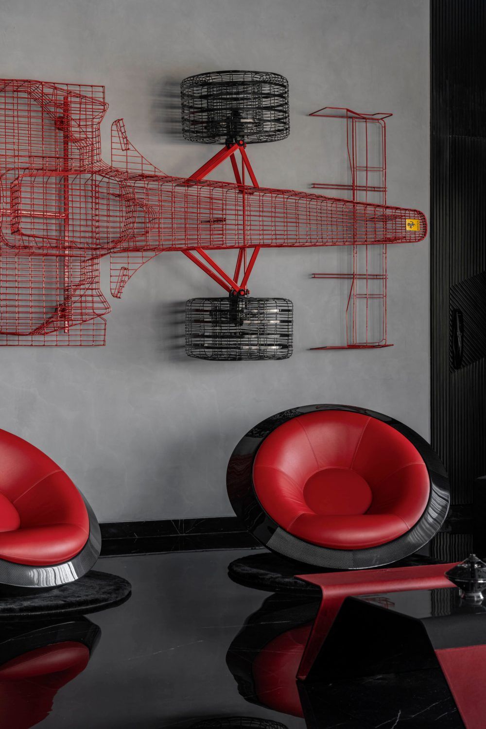 Modern lounge featuring a large red wire Formula 1 car wall installation and red leather pod chairs.
