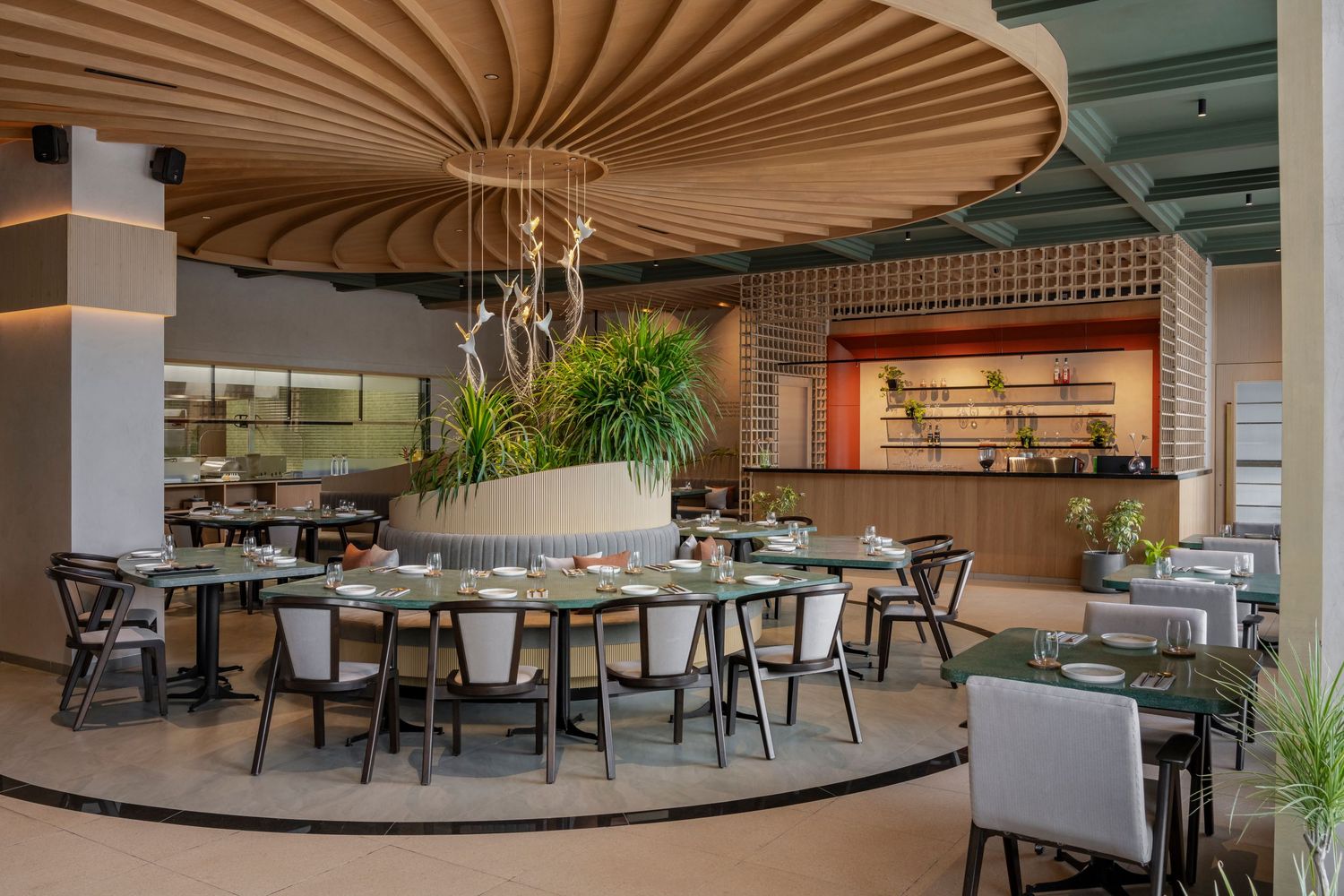 Contemporary restaurant dining room with sculptural ceiling feature, round tables, and open kitchen backdrop.