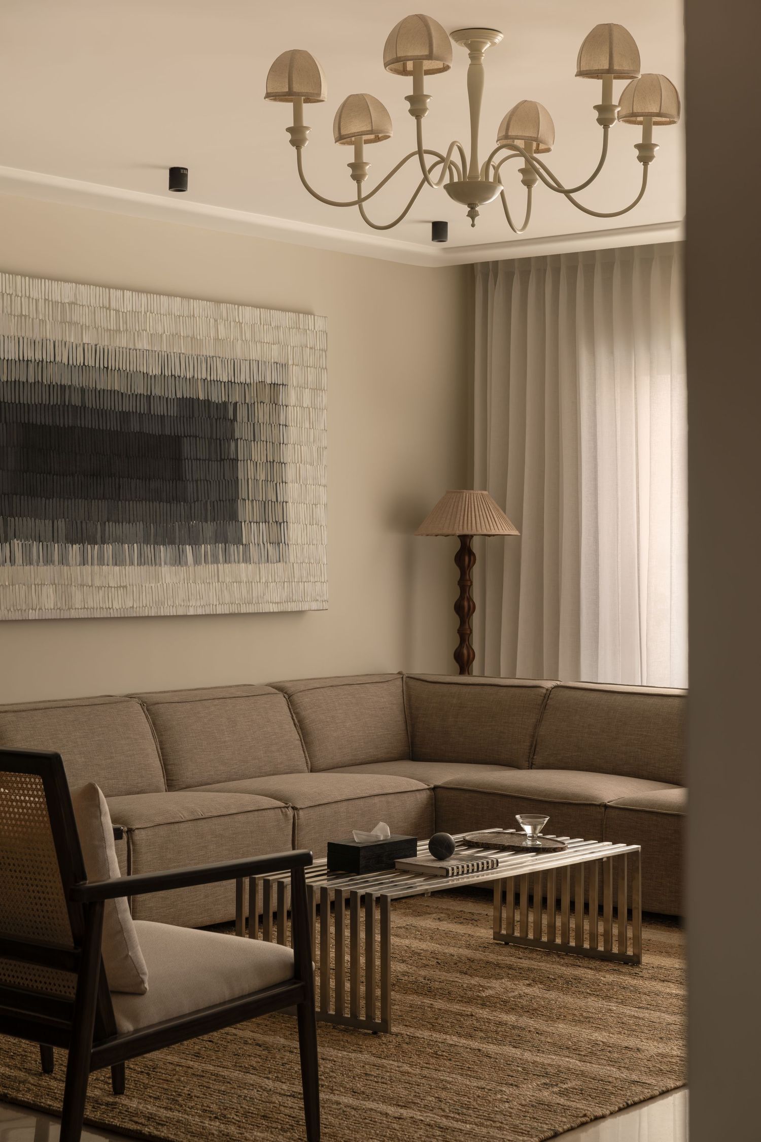 Elegant living room featuring multi-arm chandelier, corner sofa, geometric coffee table, and abstract artwork.