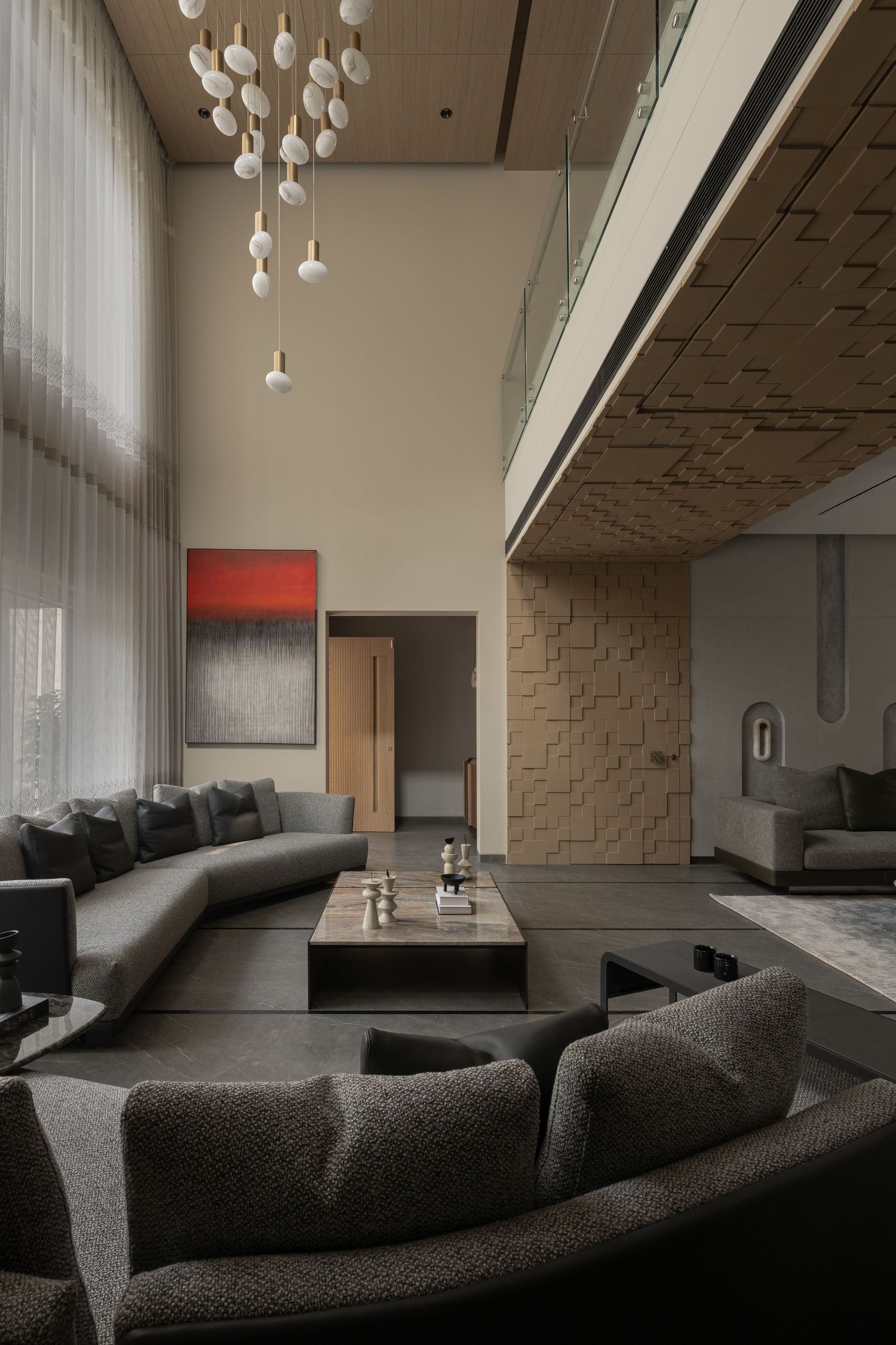 Dramatic double-height living room with globe chandelier, gray sectional sofas, red abstract art, and textured wall.