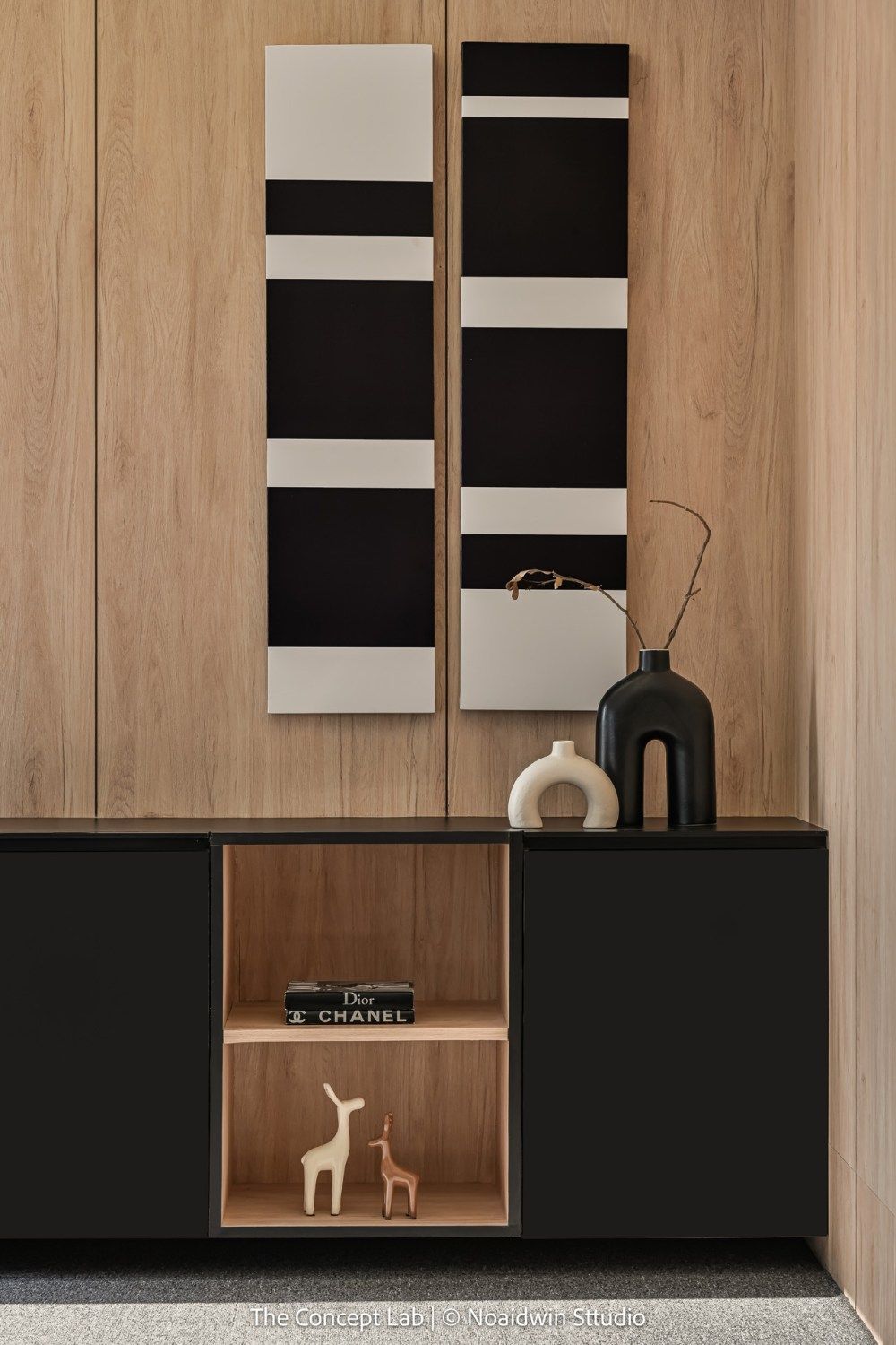 Contemporary sideboard with black and white striped wall art, Chanel books, and decorative vases on wood paneling.