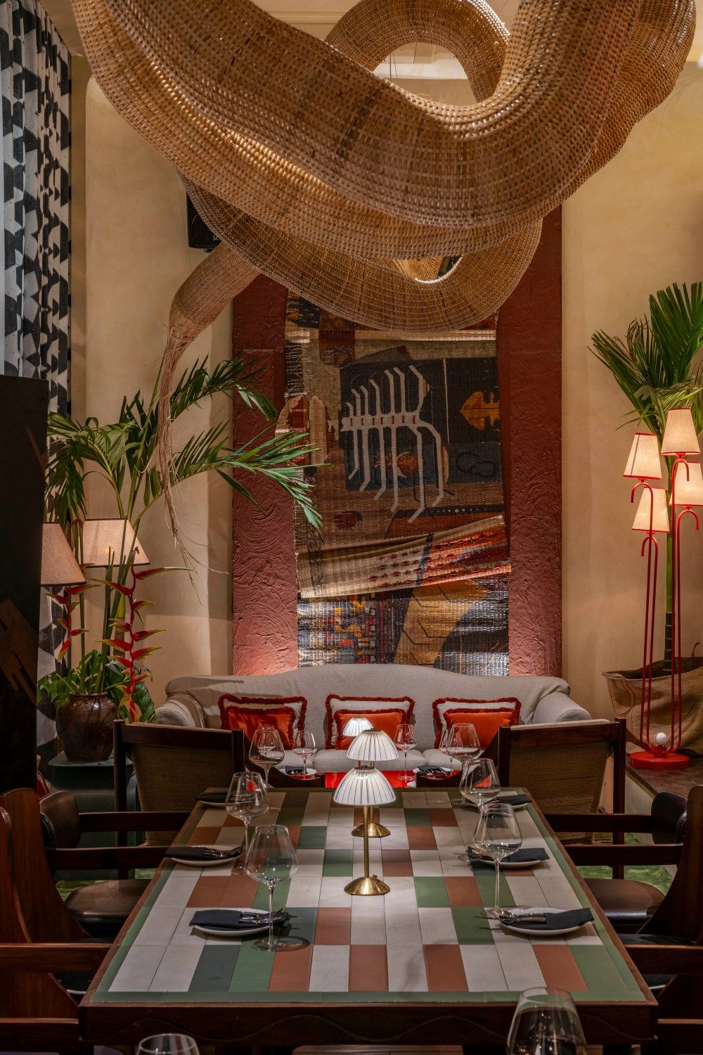 Elegant restaurant dining area with woven rattan chandelier, checkered table, red chairs, and eclectic wall art.