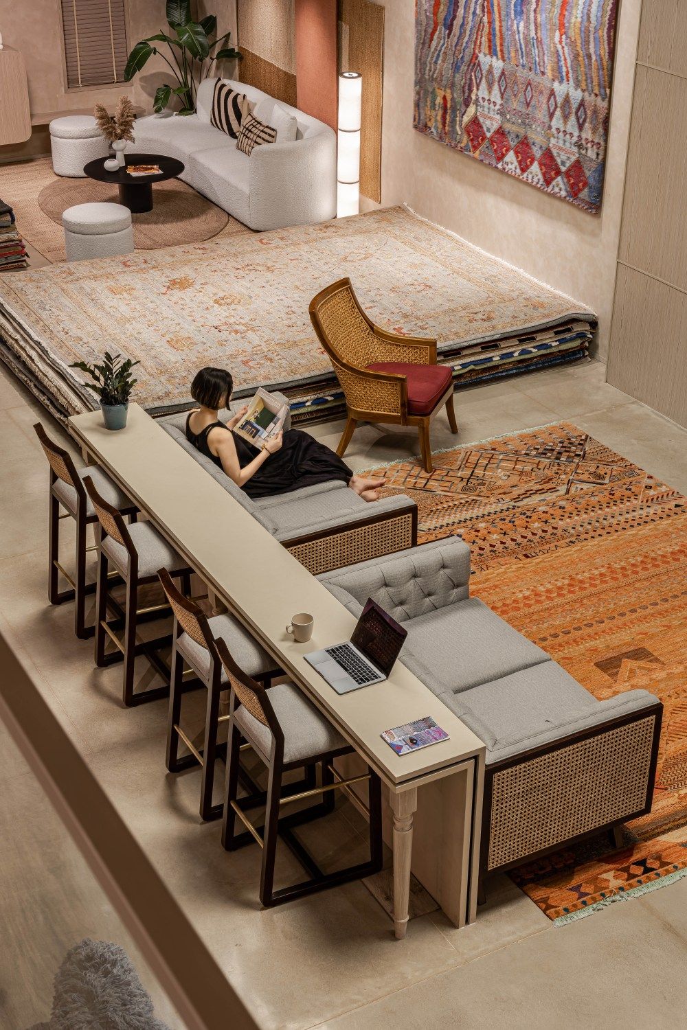 Aerial view of modern lounge with curved white sofa, person working at bar counter, and layered vintage area rugs.