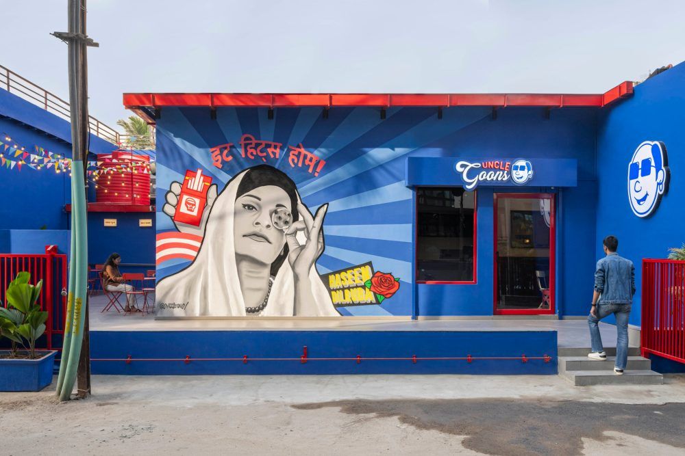 Vibrant blue building exterior with large street art mural of Indian woman and bold graphic design elements.